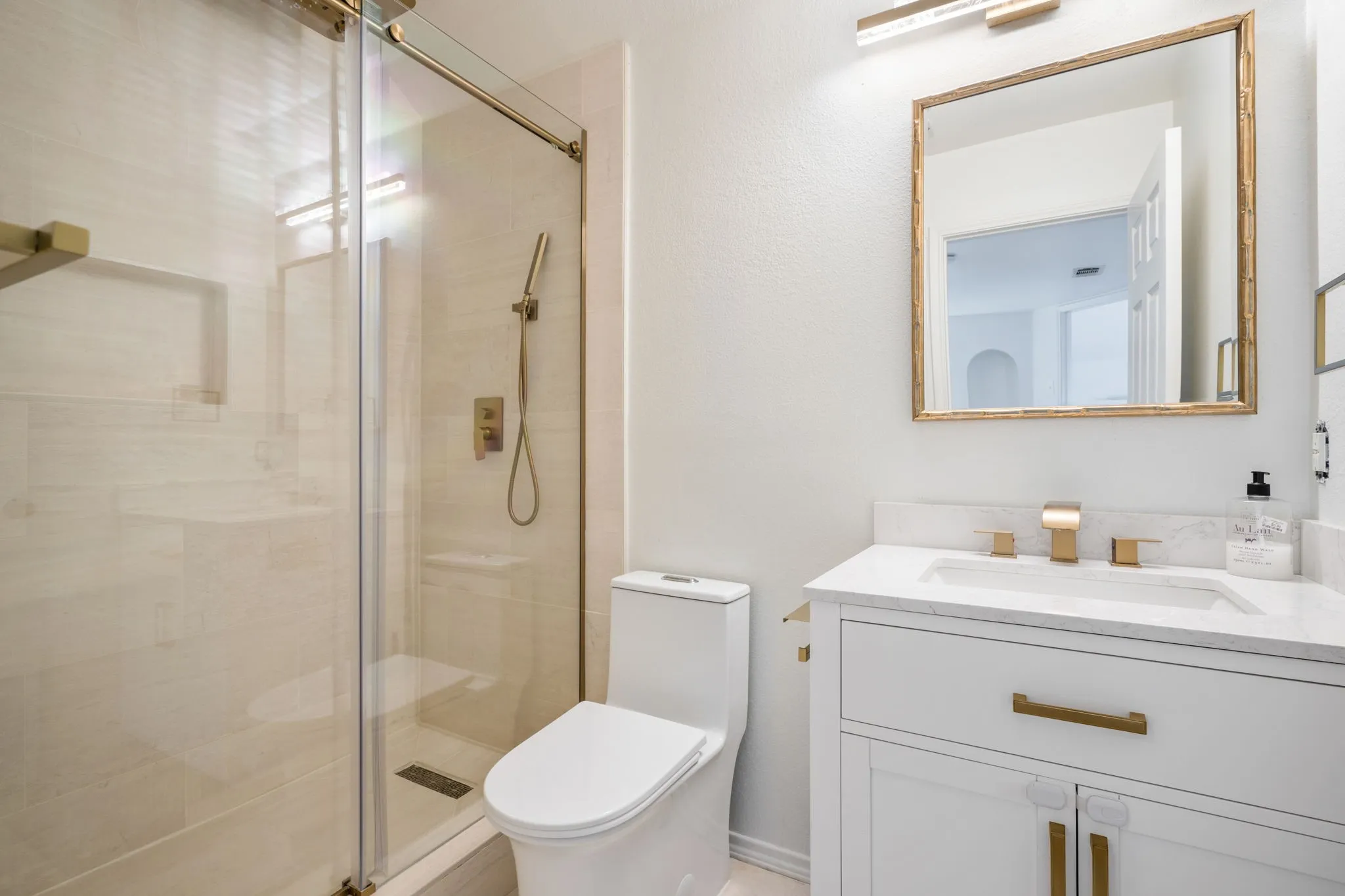 The guest bath features Italian limestone, frameless rain shower, integrated Bluetooth speakers, LED lighting, marble vanity & gold fixtures.