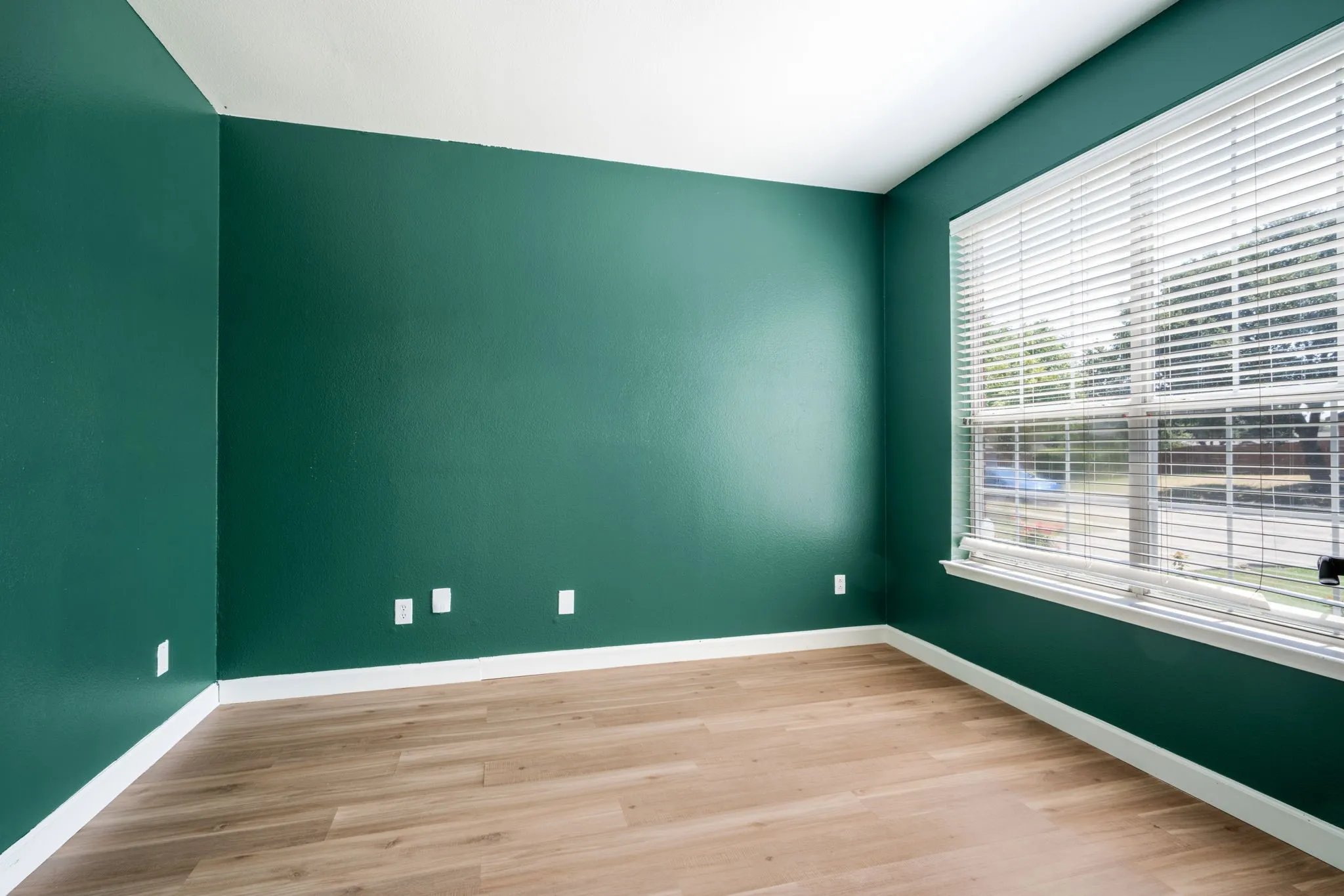 Wood-finish flooring, white baseboards, and a large window with blinds