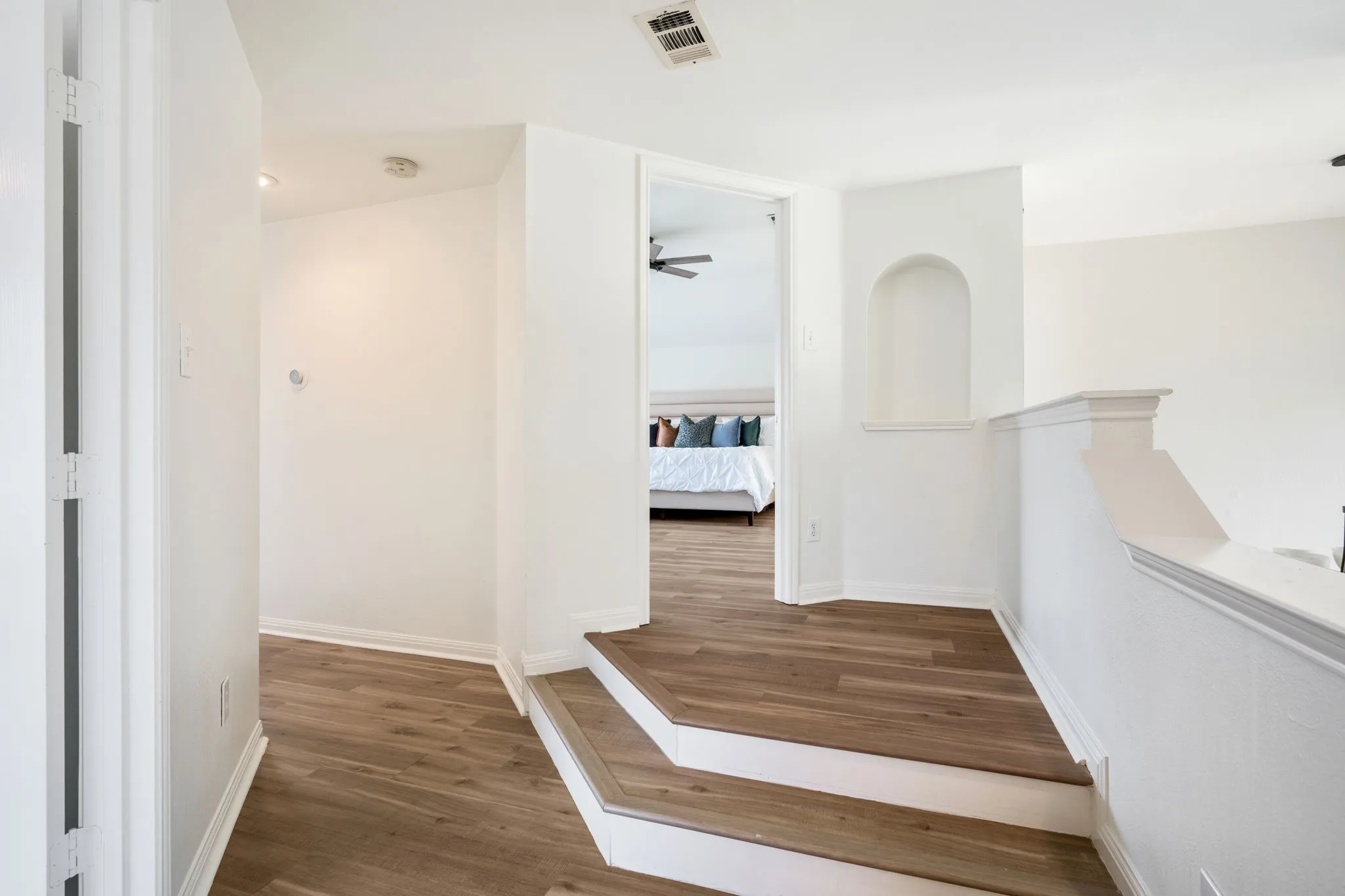 Wood-finish flooring, recessed lighting, arched wall niche, and white painted balustrade