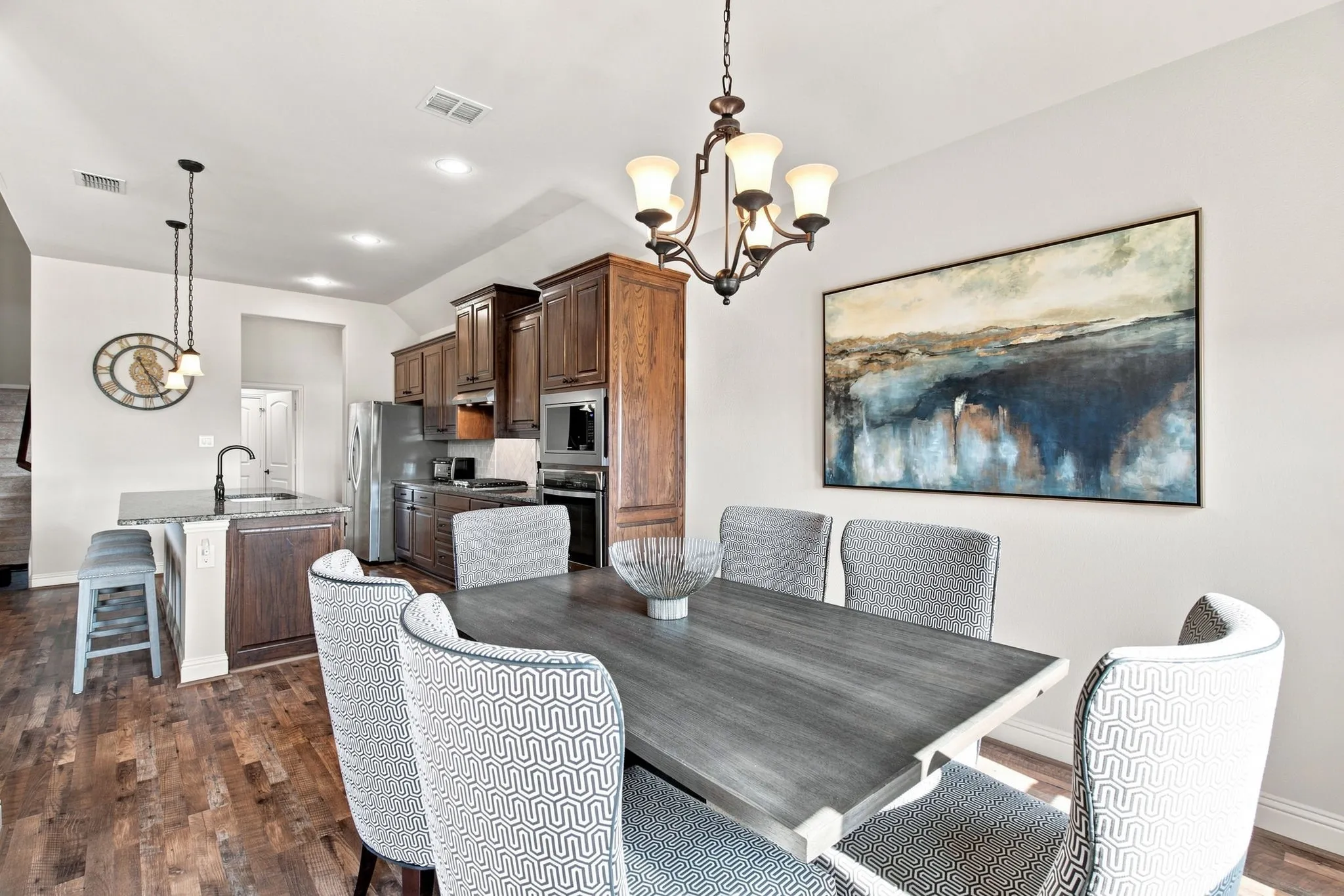 Wood-finish flooring throughout, kitchen with dark wood cabinetry and stainless steel appliances, kitchen island with built-in sink, recessed lighting, and an ornate chandelier