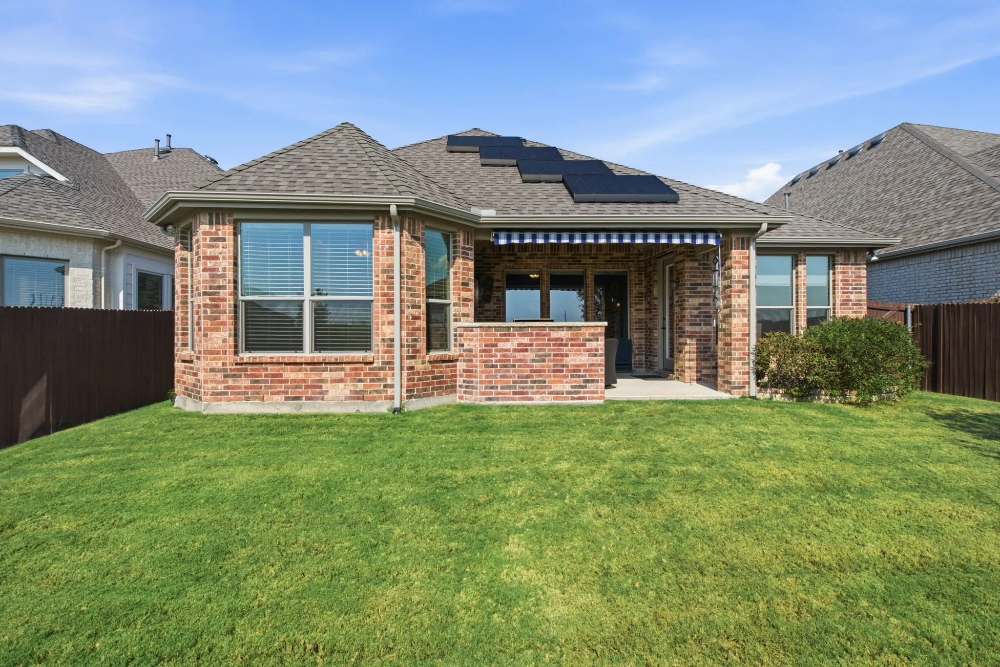 Expansive lawn with a brick exterior, covered patio with striped awning, and roof-mounted solar panels