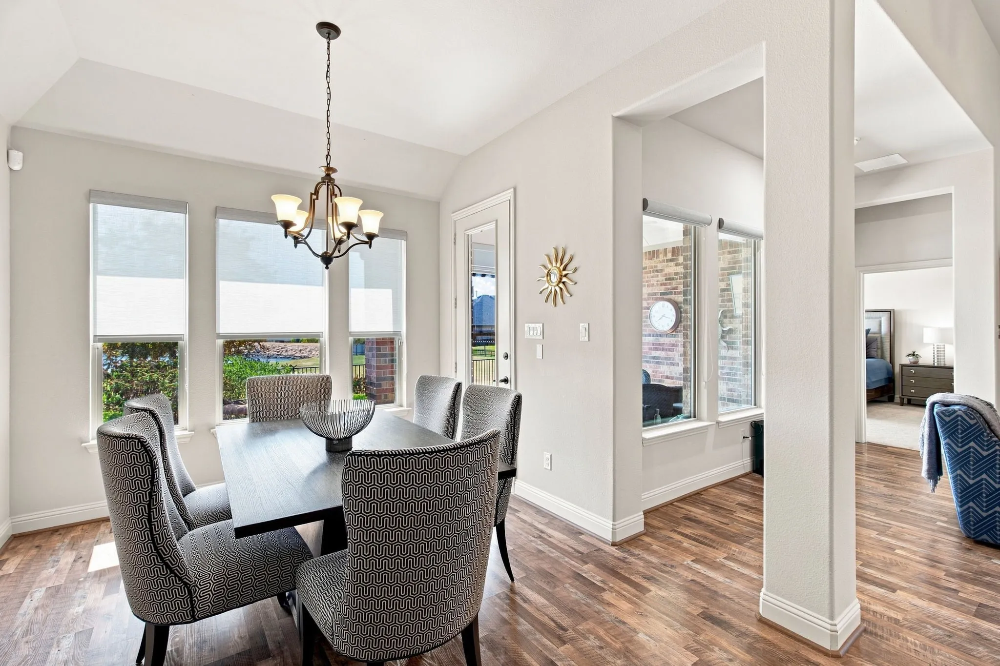 Wood-finish flooring, multiple windows with roller shades, a traditional chandelier, and architectural columns