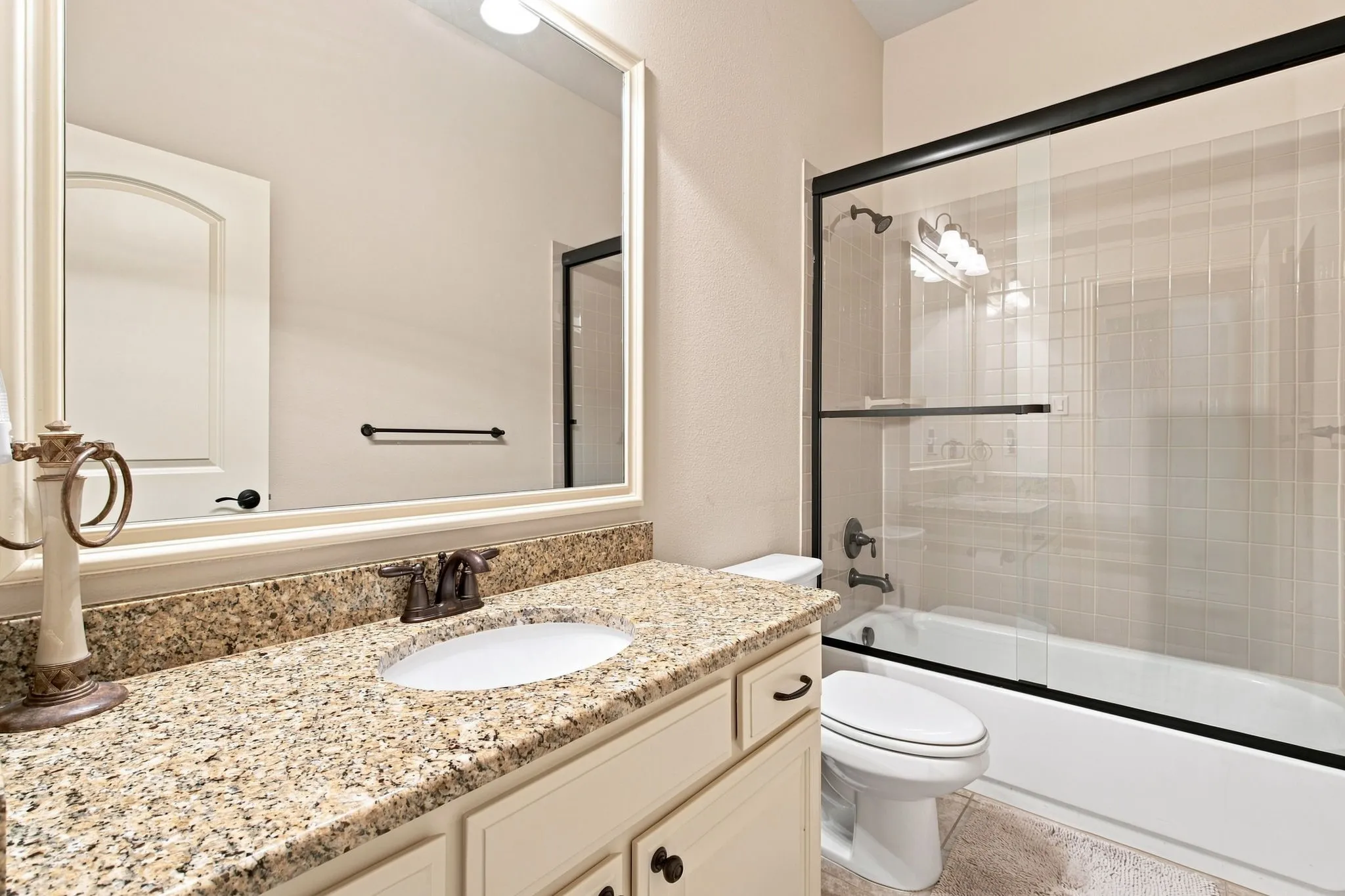 Bathroom featuring a framed mirror, a vanity with a granite countertop, an undermount sink, and a tub with a glass enclosure