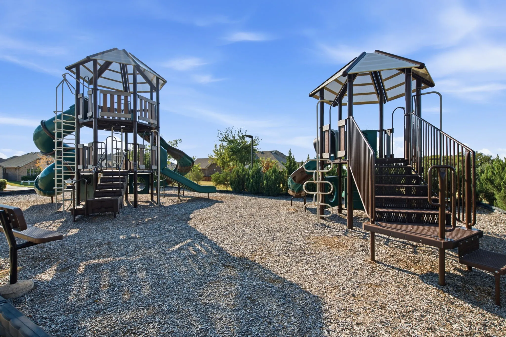 Community playground featuring two play structures, multiple slides, ladders, and protective ground covering