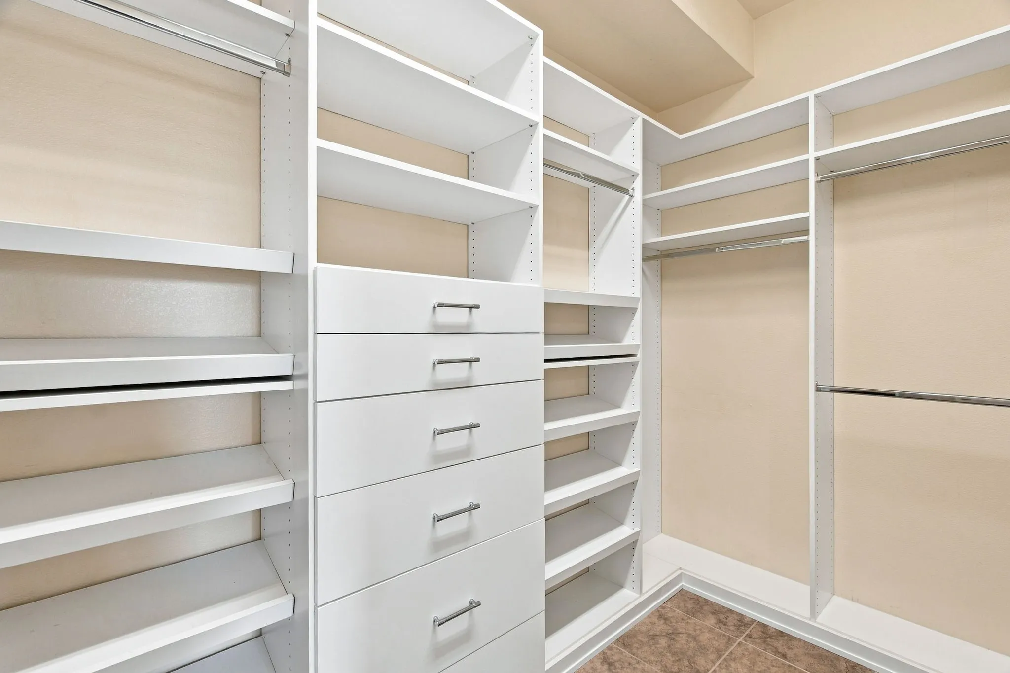 Custom closet system featuring multiple shelving units, built-in drawers with brushed nickel hardware, and ample hanging rods
