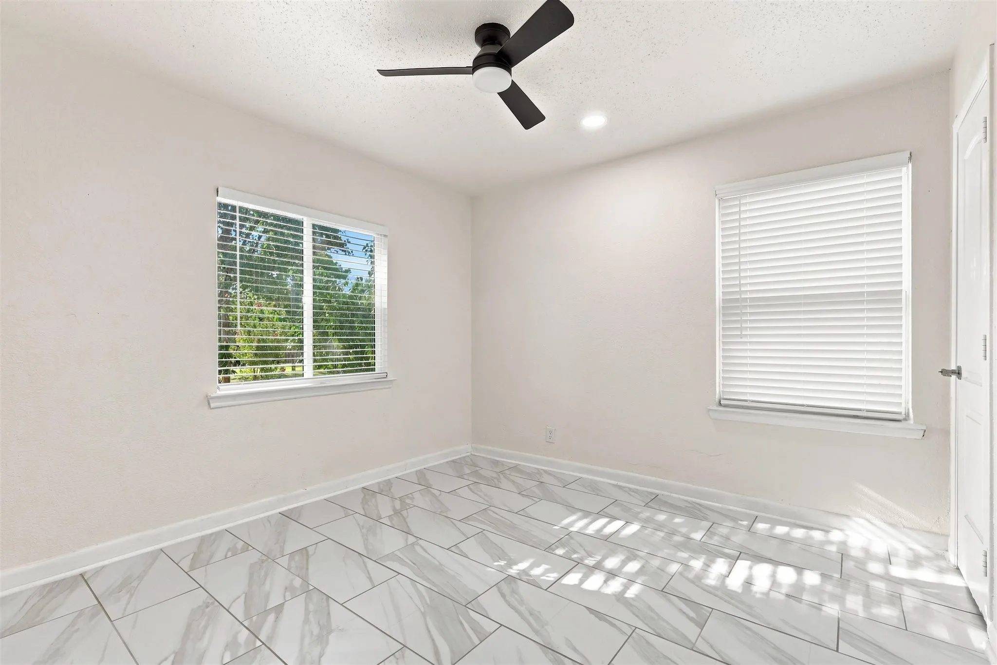 White walls with trim, ceiling fan, recessed lighting, two windows with blinds, and large format tile flooring