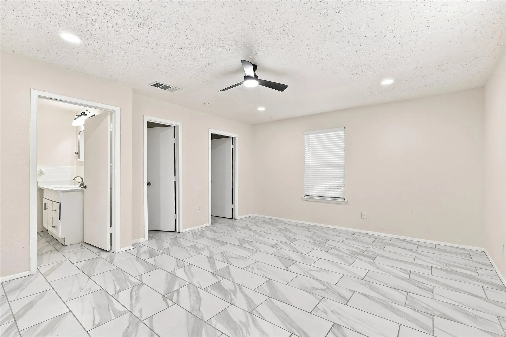 Spacious room with light-toned walls, white tile flooring, and a ceiling fan