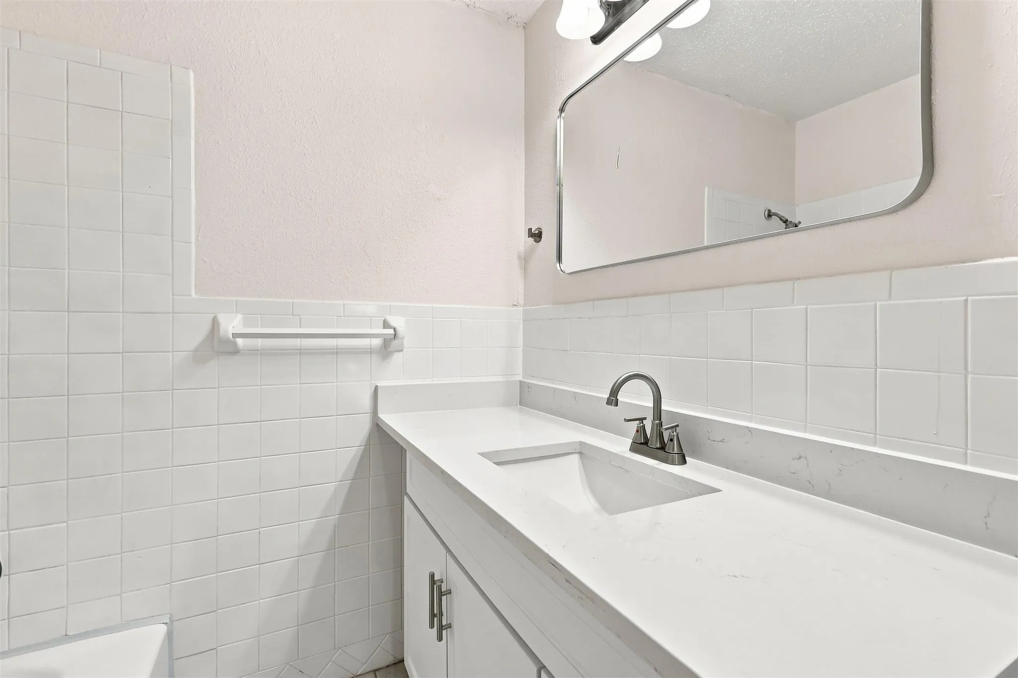 Clean-lined bathroom featuring white subway tile walls, a white vanity with integrated sink and ample countertop space, chrome faucet fixture, and a framed mirror with polished metal trim