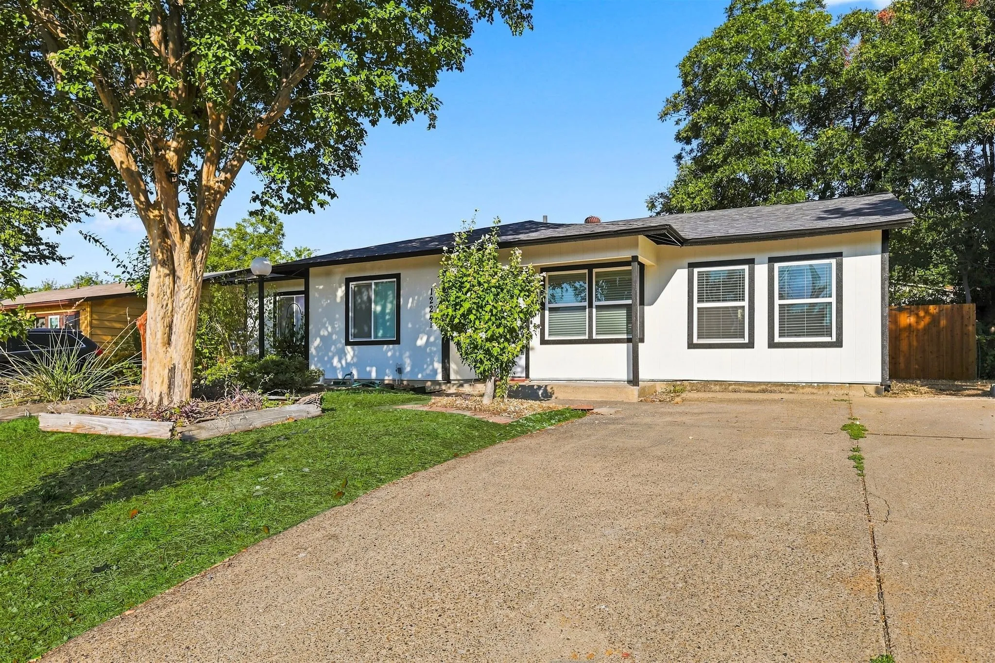 Single-story residence featuring a white exterior with dark trim windows, an asphalt shingle roof, and an attached driveway