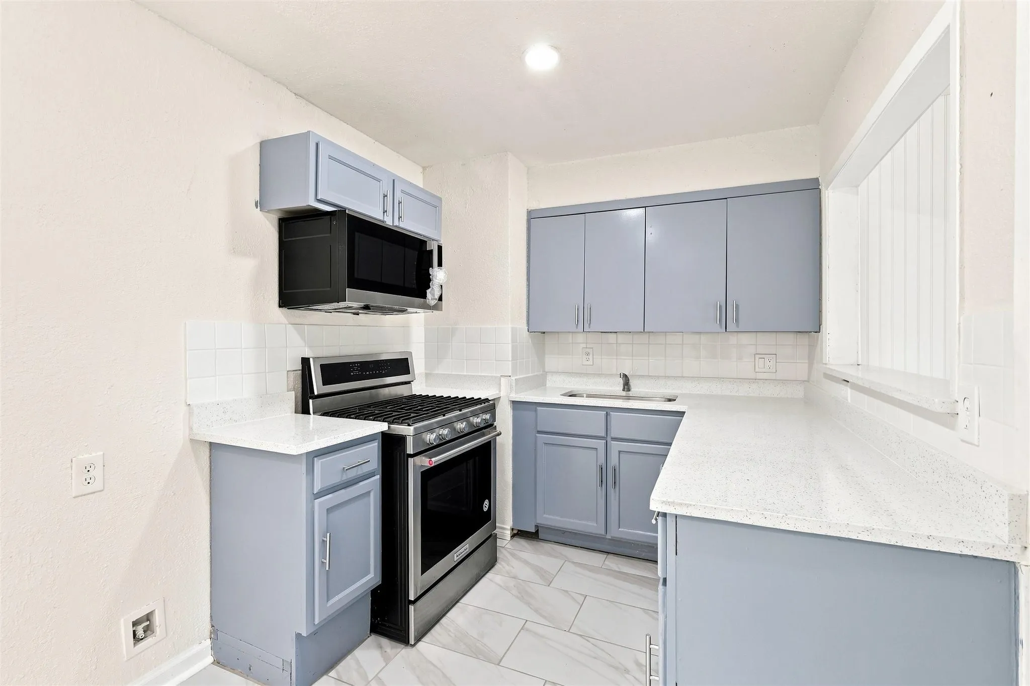 Kitchen with light blue cabinetry, white countertops, tile flooring, stainless steel range, and an over-the-range microwave