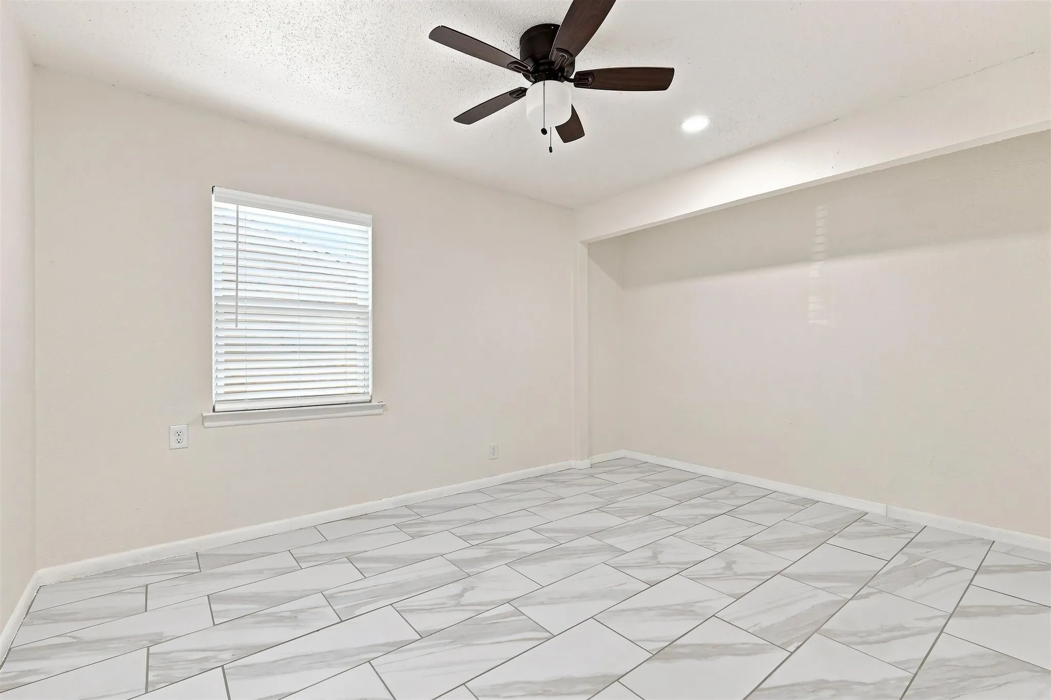 Spacious room featuring large format tile flooring, a window with horizontal blinds, a ceiling fan with integrated lighting, and recessed ceiling lighting