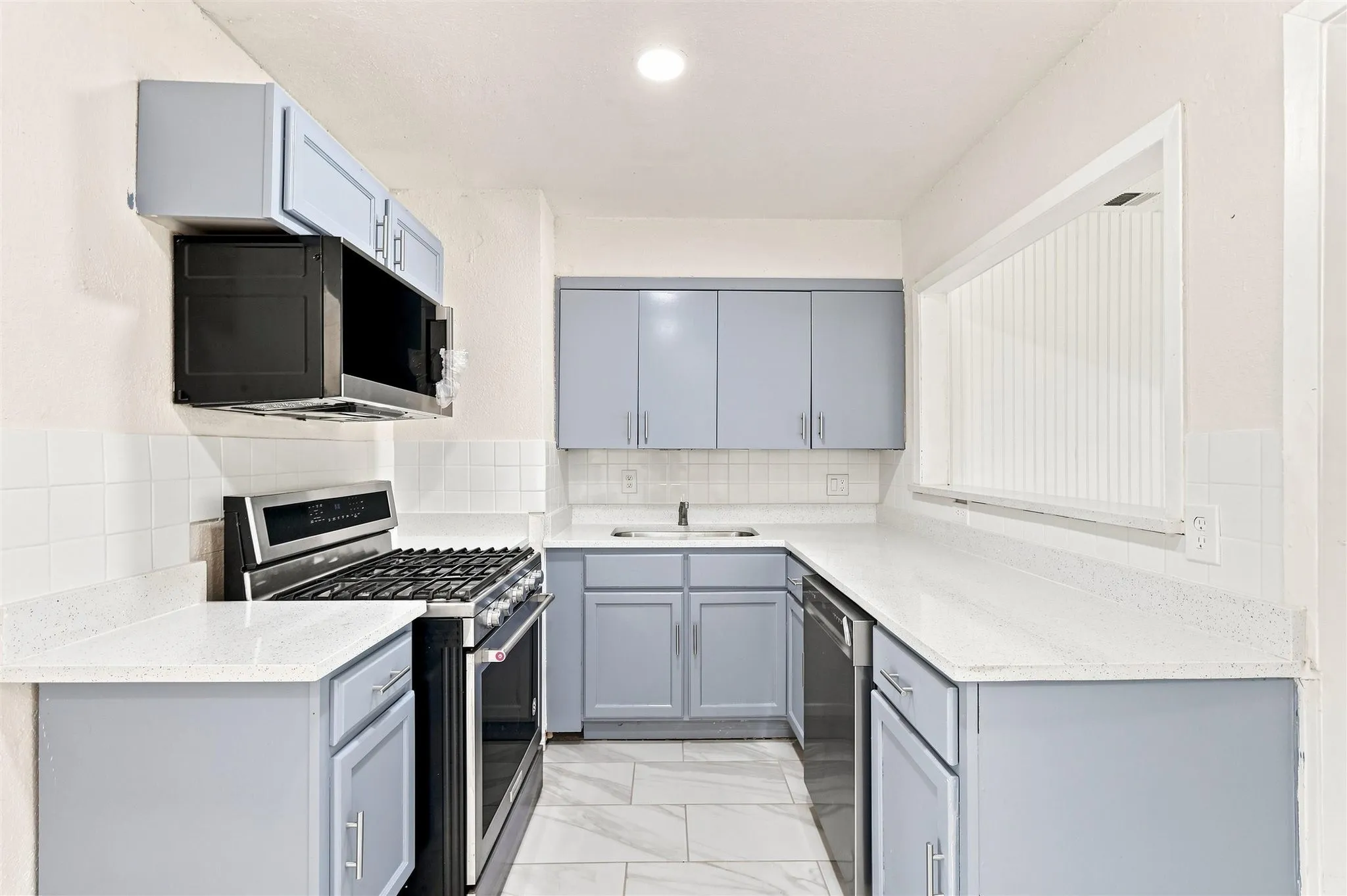 U-shaped kitchen featuring light blue cabinetry, white countertops, tile flooring, and white subway tile backsplash