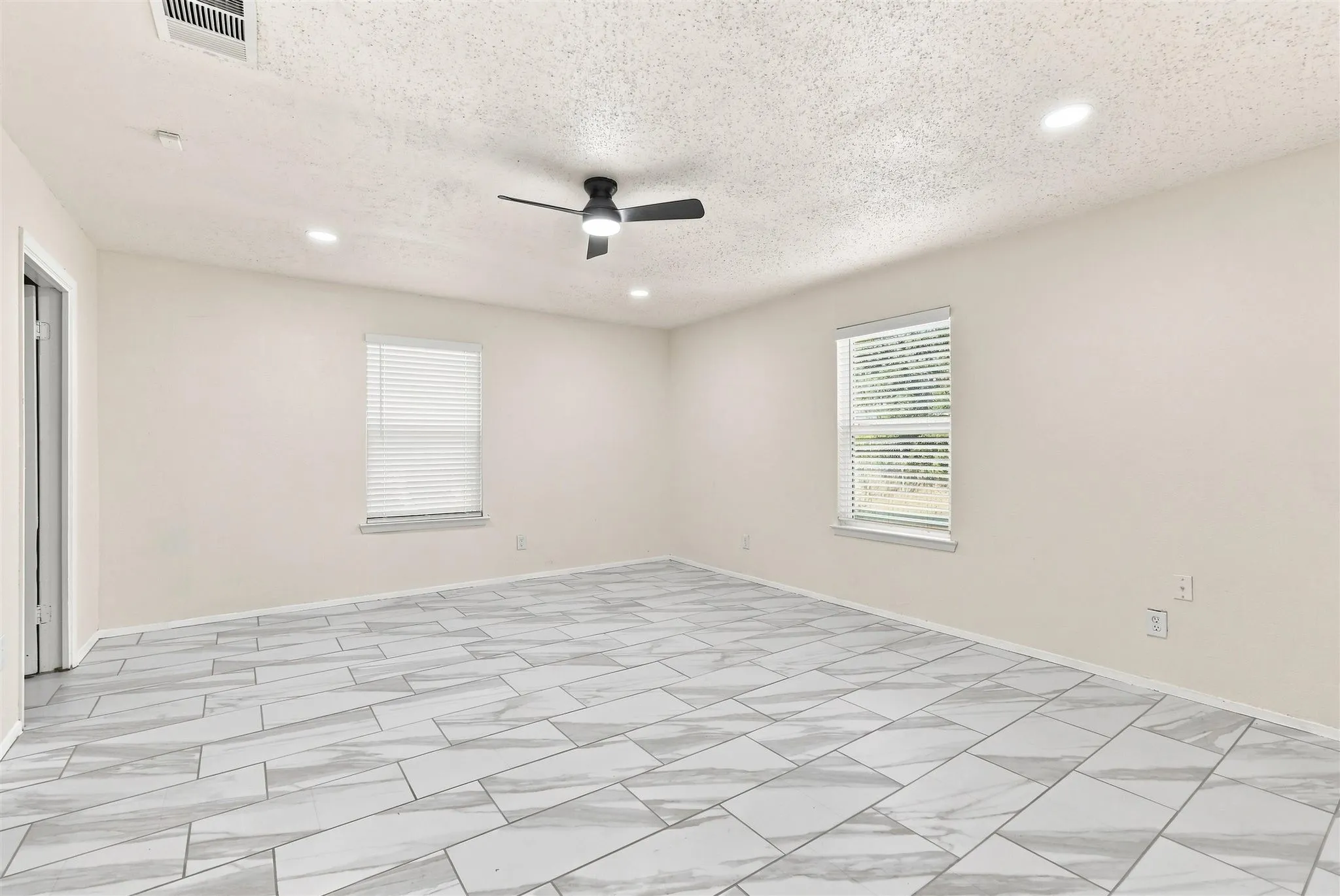 Light-toned walls with recessed lighting, two windows with blinds, and a ceiling fan