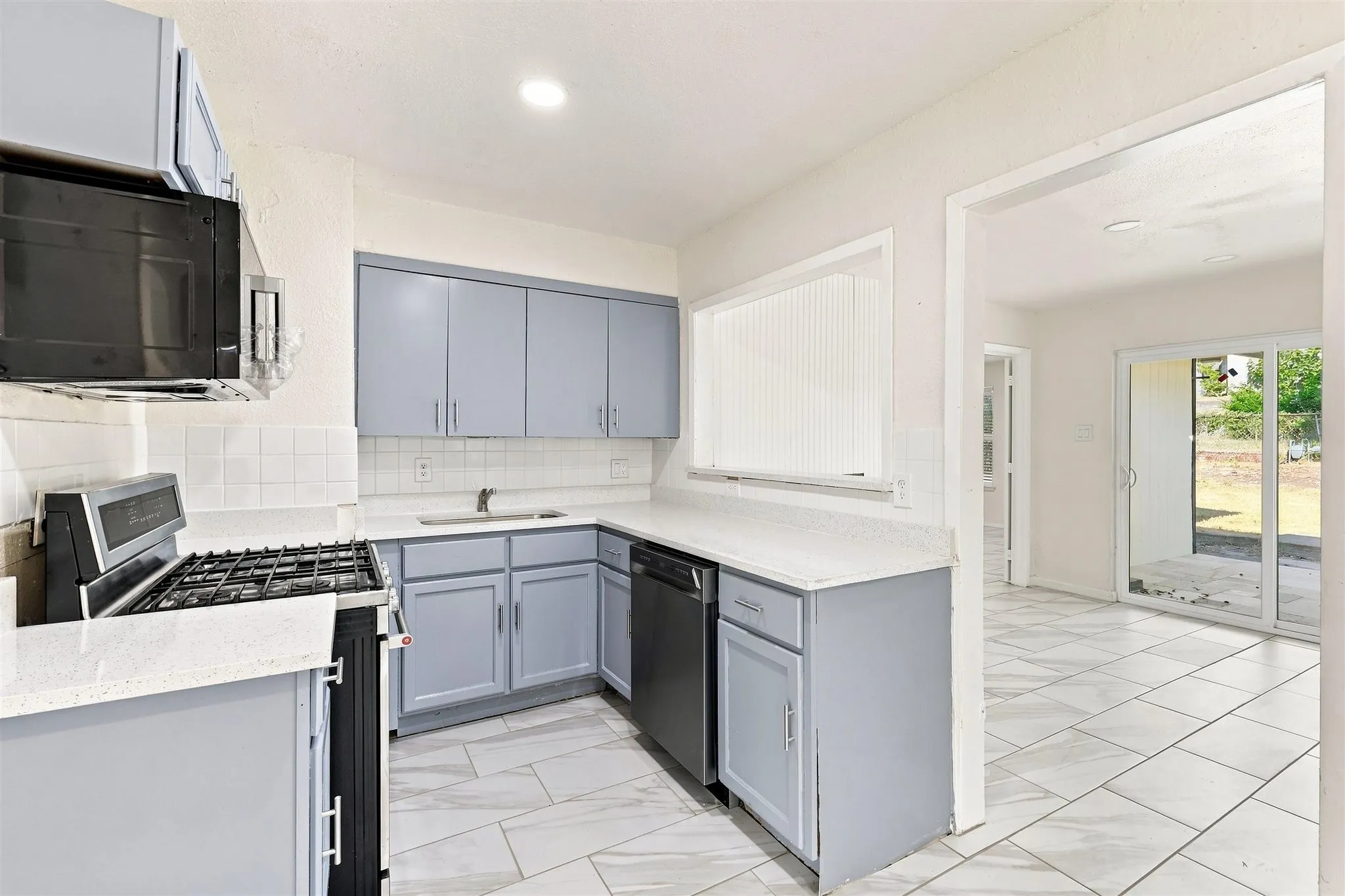 Kitchen featuring blue-grey cabinetry, white countertops, tile backsplash, and stainless steel appliances
