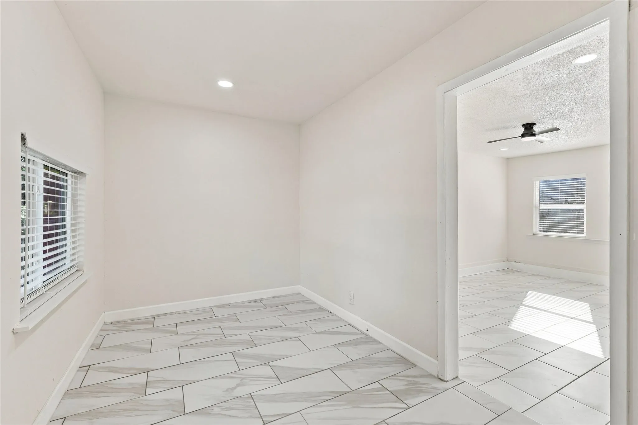 White interior walls with recessed lighting, tile flooring, window with blinds, and doorway to additional room with ceiling fan