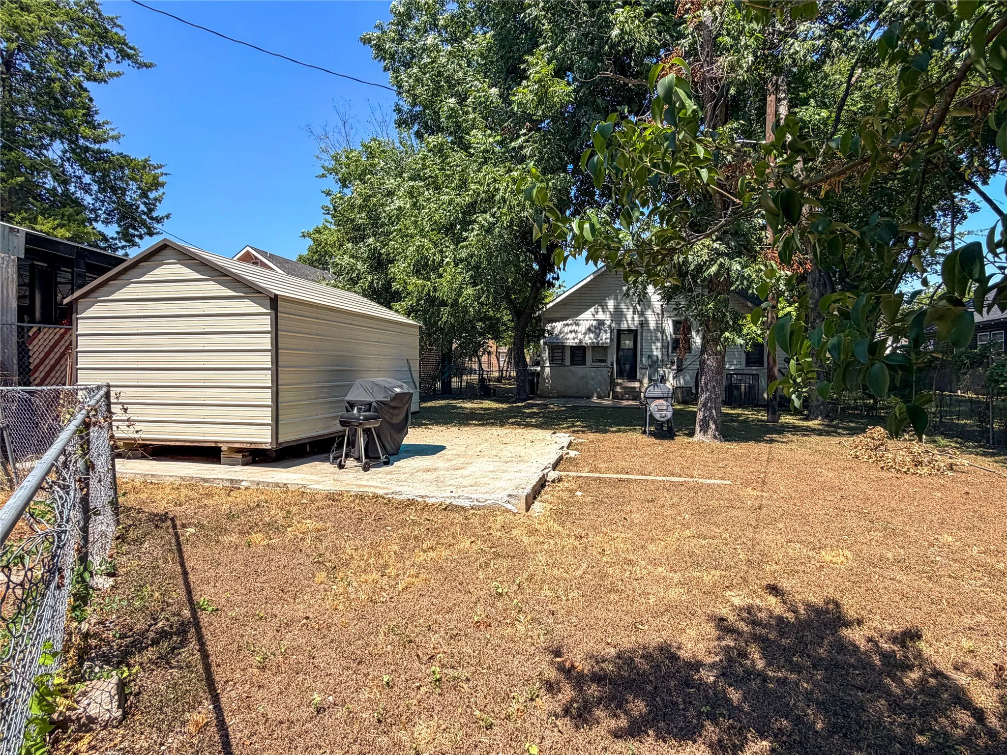 Spacious backyard with a detached storage shed, chain-link fencing, and mature trees