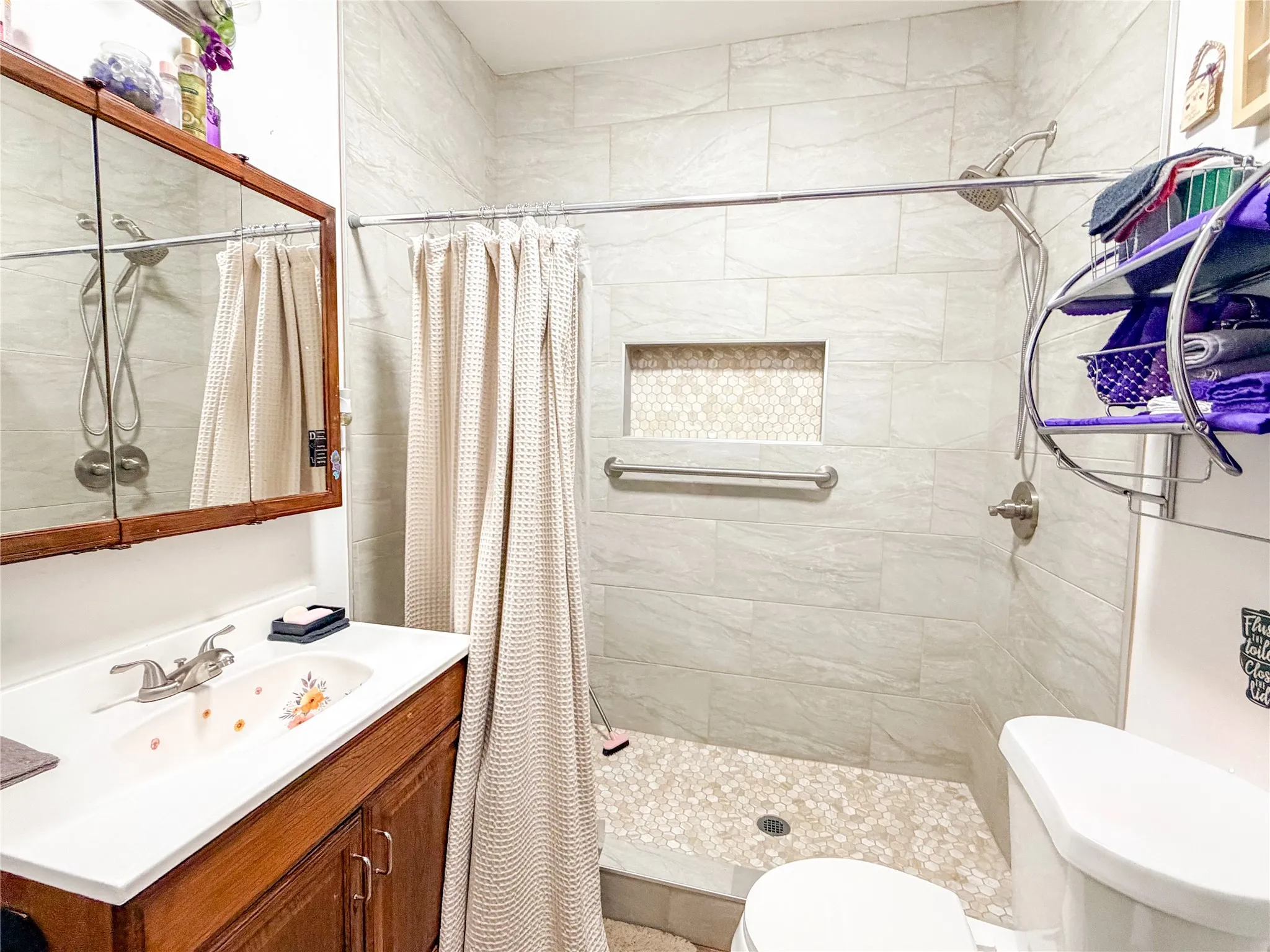 Tiled shower with a recessed niche and textured pebble flooring, featuring a wall-mounted grab bar and a brushed nickel shower fixture