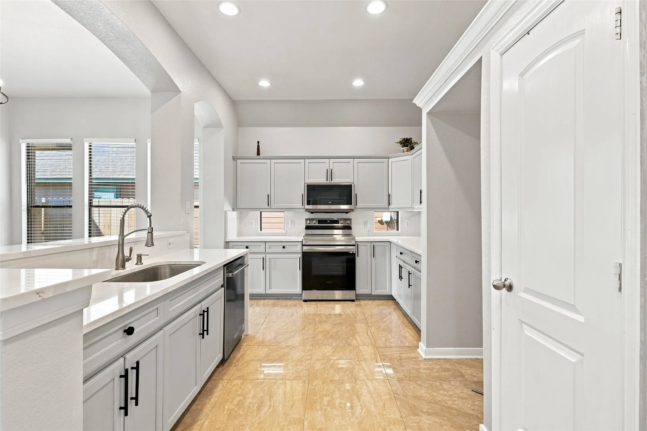 Kitchen featuring light gray cabinetry with black hardware, stainless steel appliances, light-toned countertops, and a tile backsplash