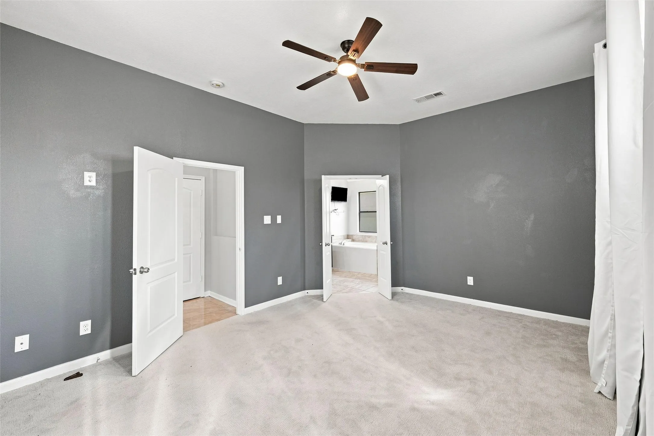 Spacious room featuring carpeting, a ceiling fan, and access to a separate area with a built-in vanity