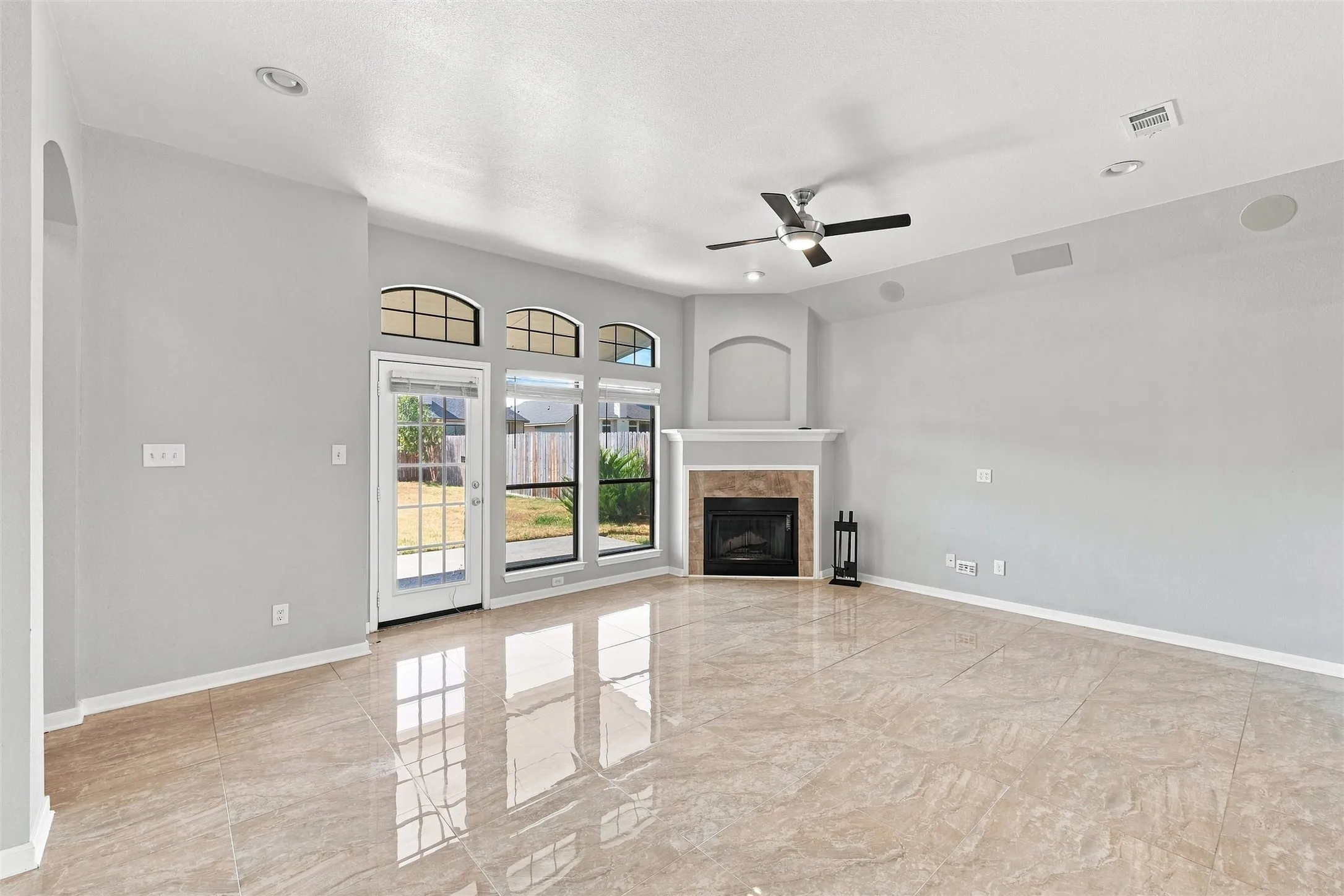 Spacious room featuring large format tile flooring, a corner fireplace with a mantel, a ceiling fan, and multiple windows with arched transoms