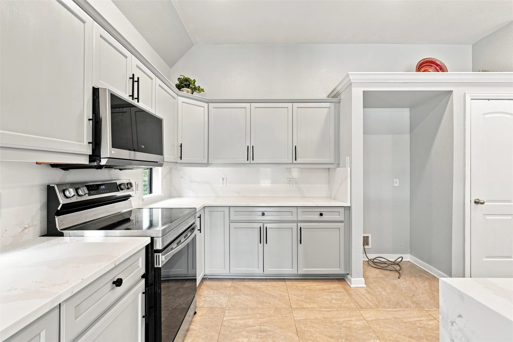 Kitchen featuring light-toned cabinetry, light countertops, integrated stainless steel appliances, a tiled backsplash, and tile flooring