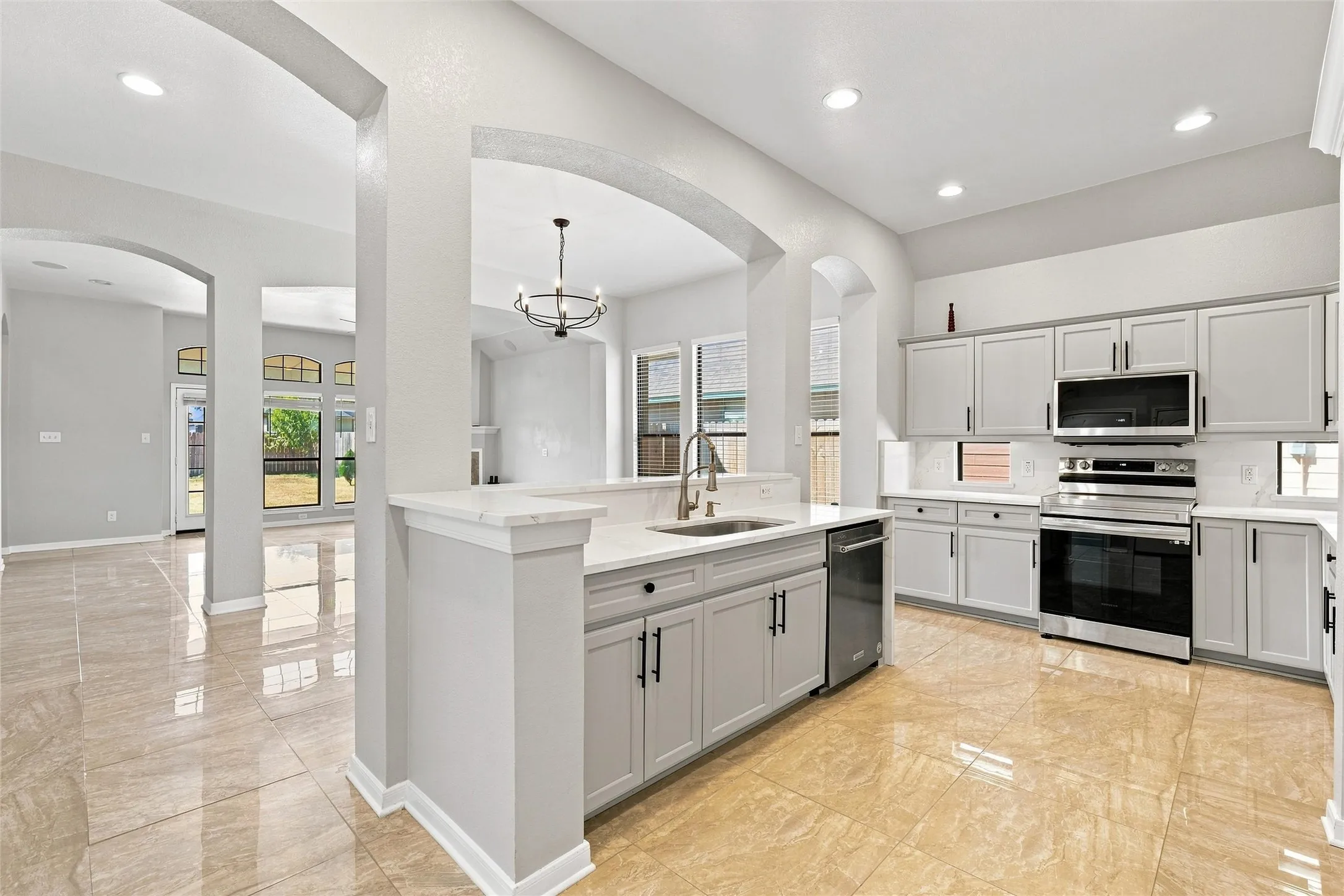 Kitchen featuring light grey cabinetry, stainless steel appliances, a center island with sink, and solid surface countertops