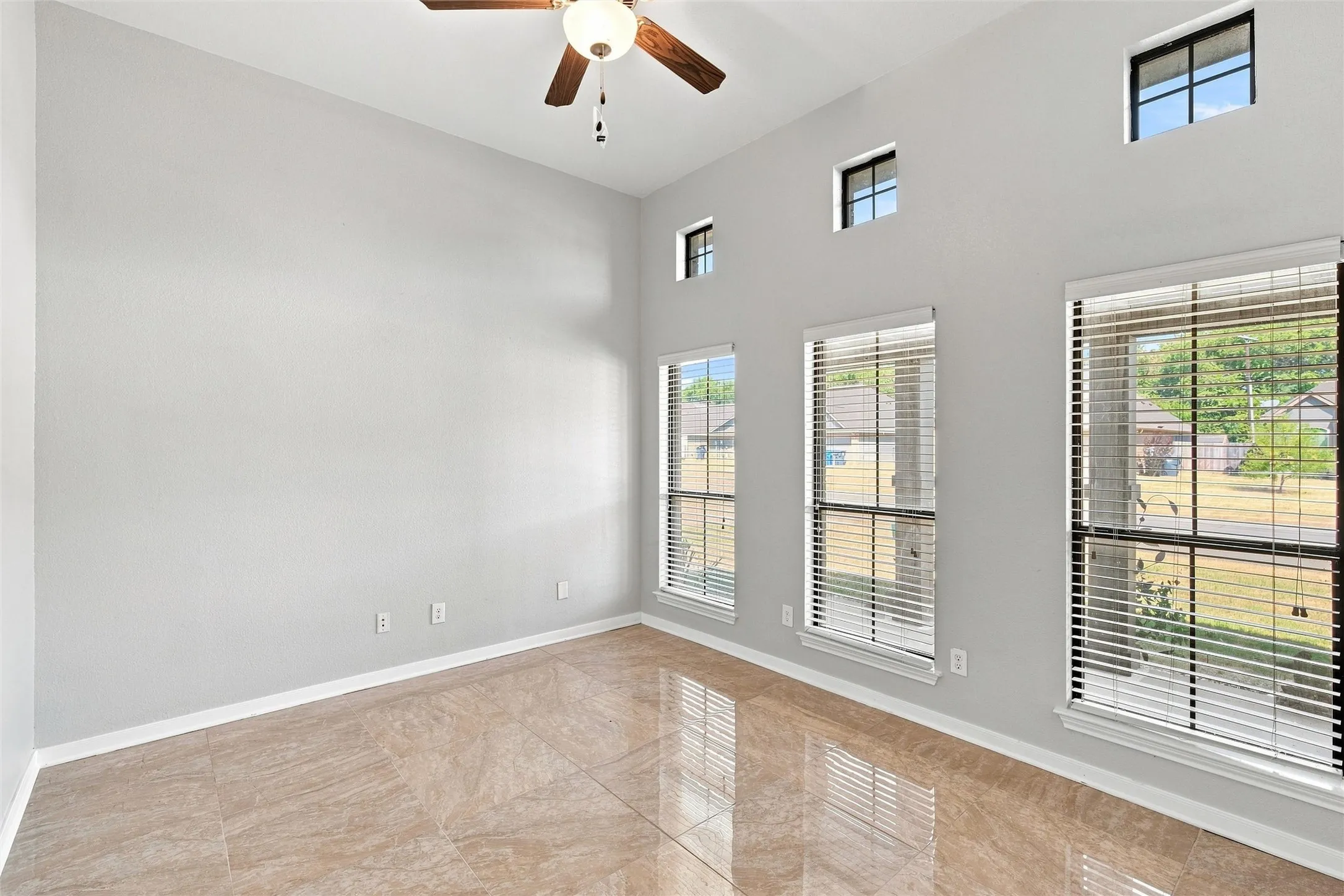 High vaulted ceiling with a ceiling fan, multiple transom windows, and full-height windows, complemented by large format tile flooring