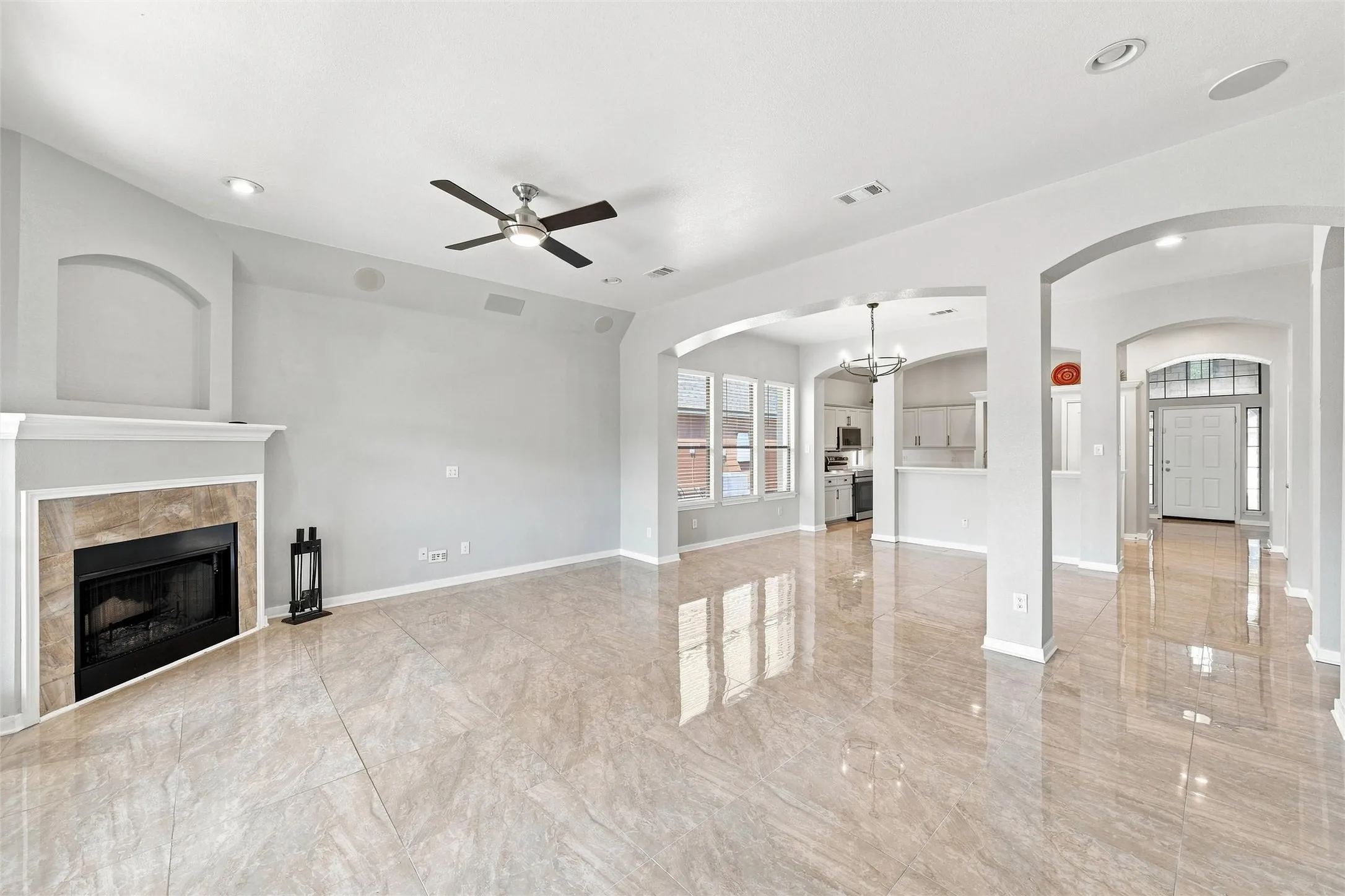 Glossy tile flooring, fireplace with stone surround, recessed lighting, ceiling fan, and arched doorways