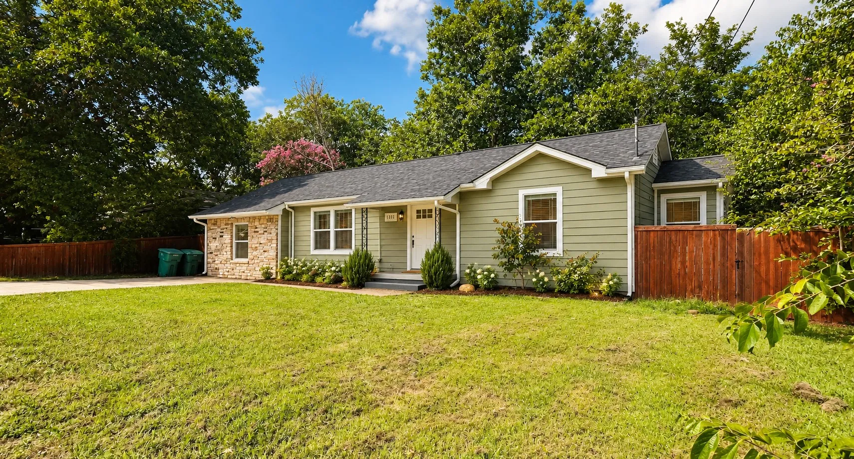 Light green siding exterior with brick accents, dark shingle roof, white trim windows, and a manicured front lawn