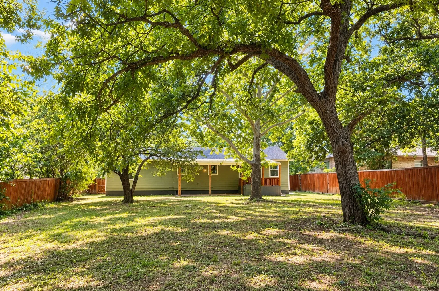 Expansive backyard with a manicured lawn, established trees, and a privacy fence