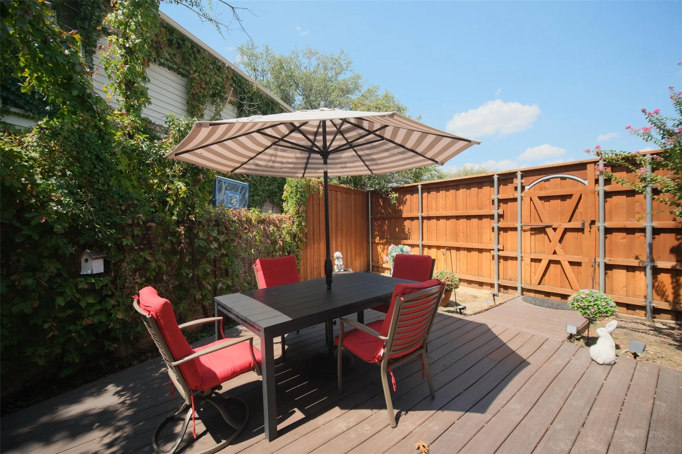 Expansive wood-finish deck with a privacy fence, lush climbing greenery, and a distinct fence gate