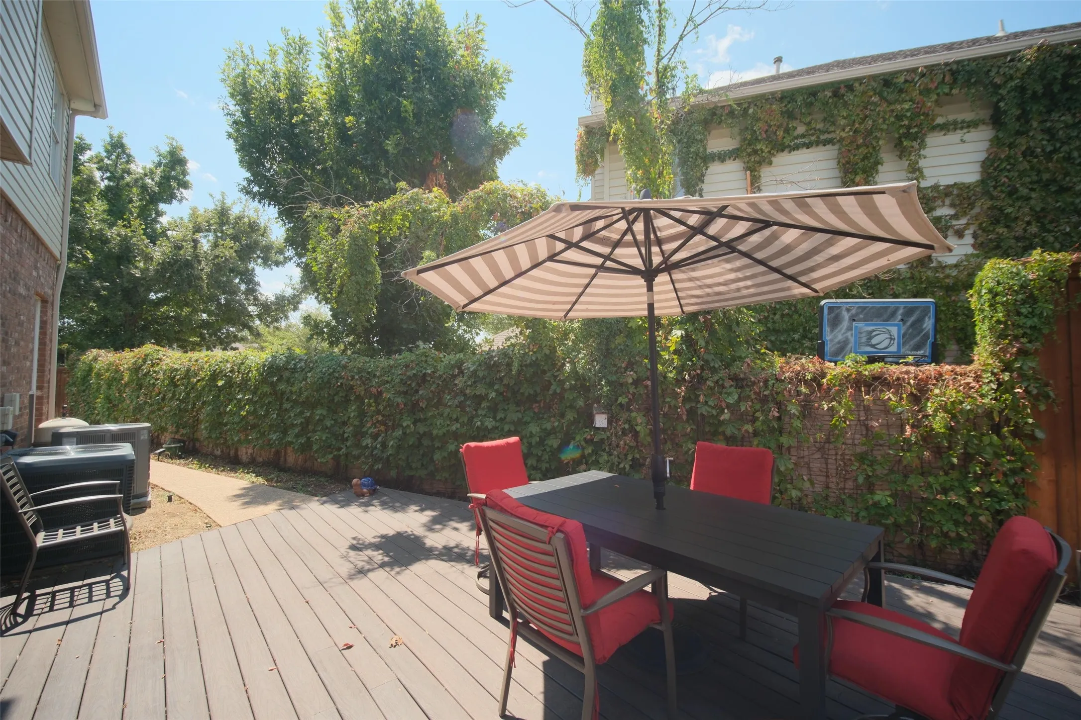 Expansive deck area with wood-finish flooring, bordered by a substantial privacy hedge