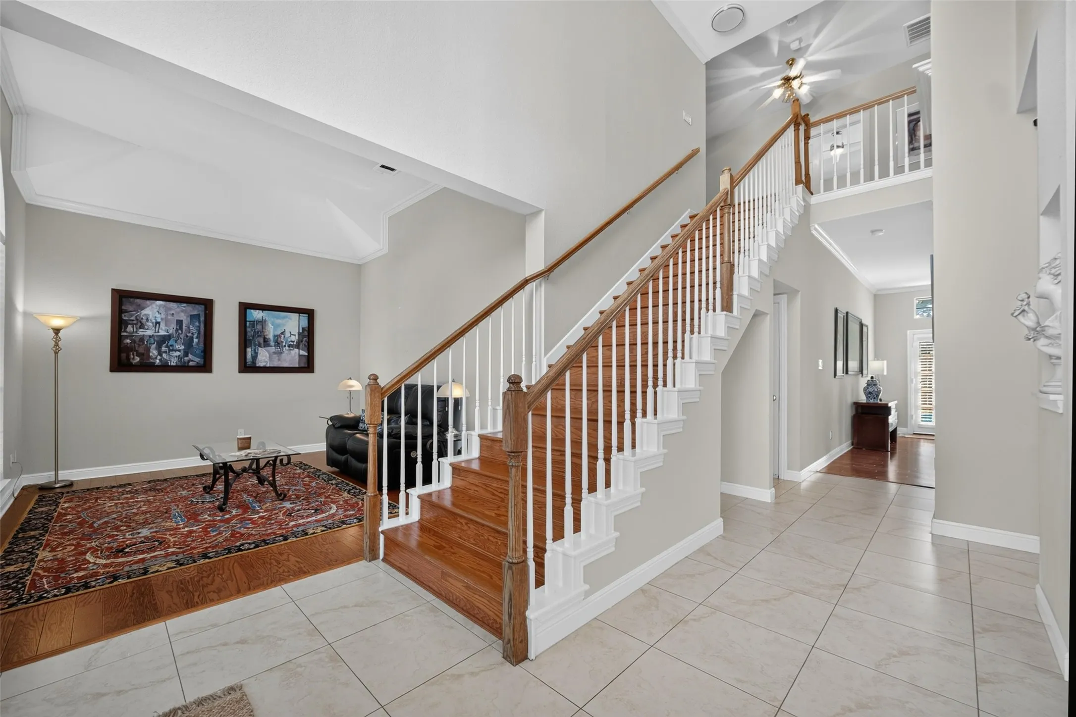 Two-story foyer with tile flooring, a prominent wooden staircase with white balusters, and a vaulted ceiling