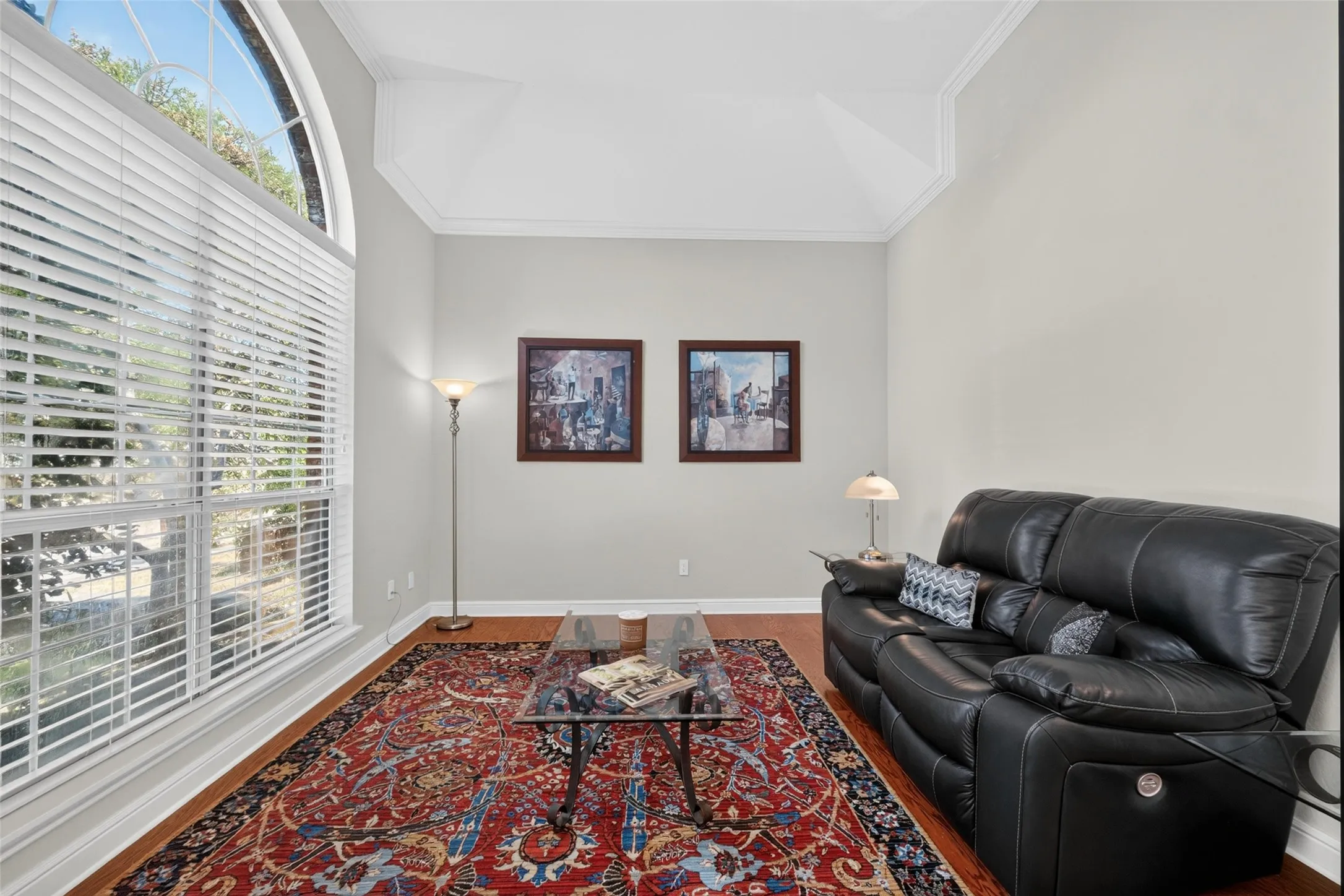 Tray ceiling with crown molding, tall arched window, white blinds, and wood-finish flooring