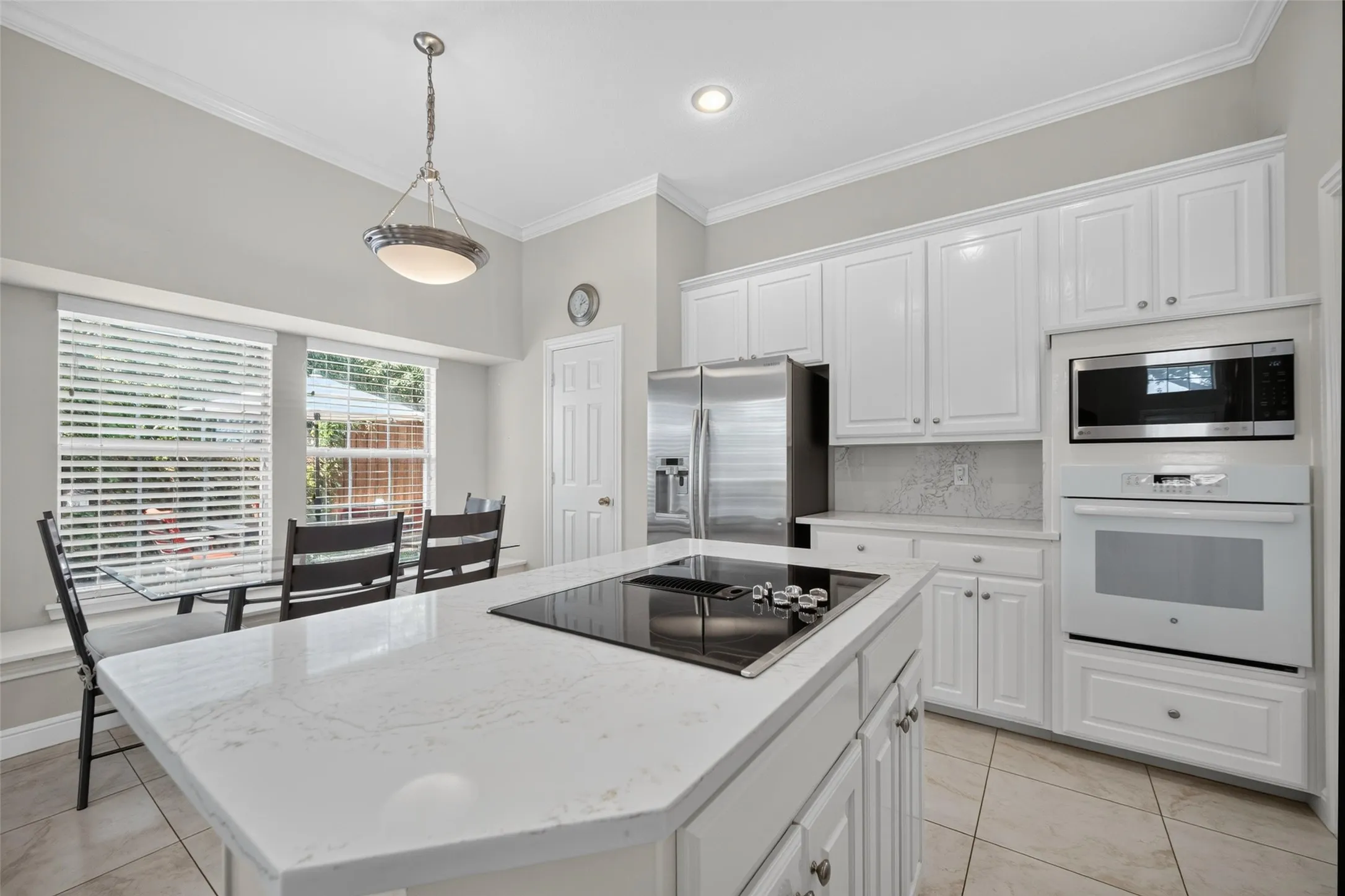 Kitchen featuring a large center island with cooktop, white cabinetry, stainless steel refrigerator, and built-in microwave and oven