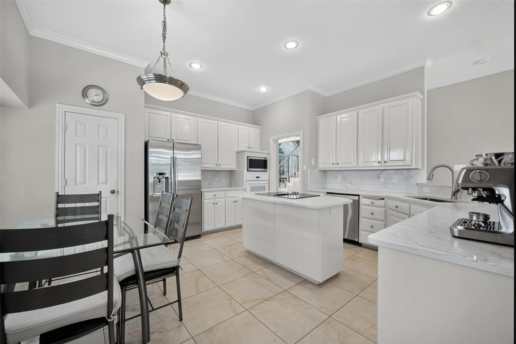 Kitchen featuring white cabinetry, light-toned tile flooring, stainless steel appliances, a center island with a cooktop, and light-toned countertops