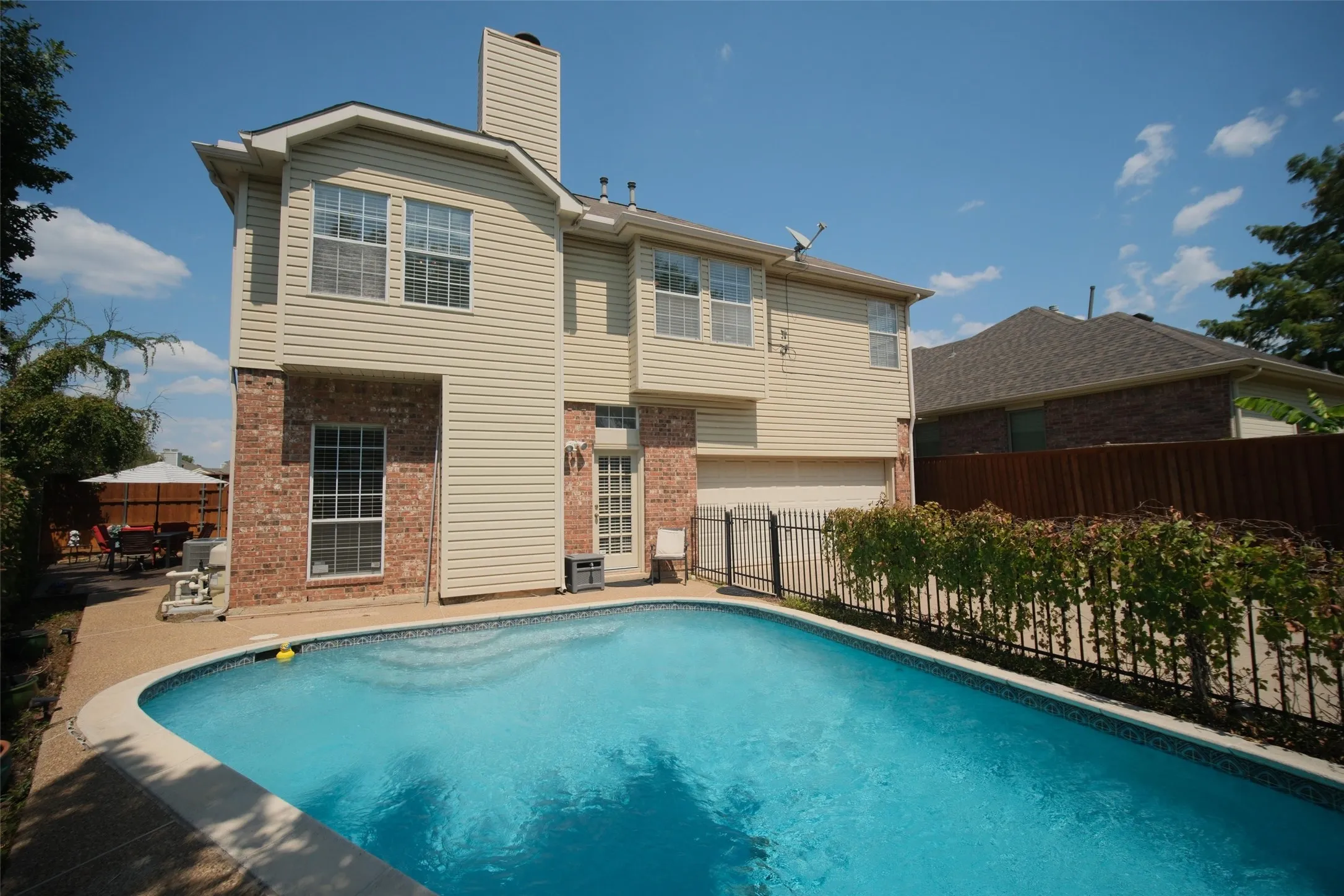 Brick and siding exterior featuring multiple windows, an outdoor swimming pool with surrounding concrete patio, and a privacy fence
