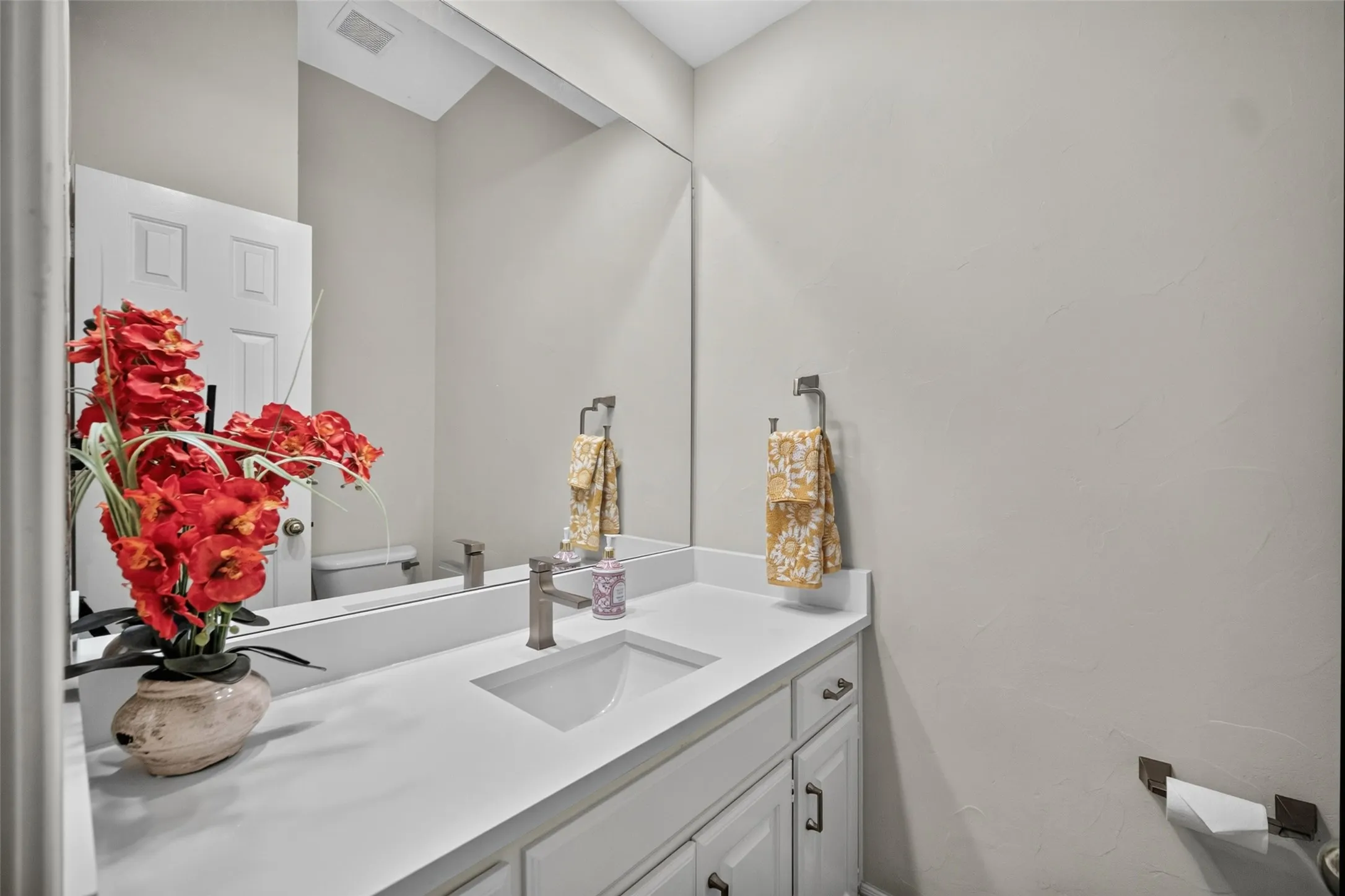 Vanity with an integrated sink, brushed nickel faucet, full-width mirror, and white cabinetry