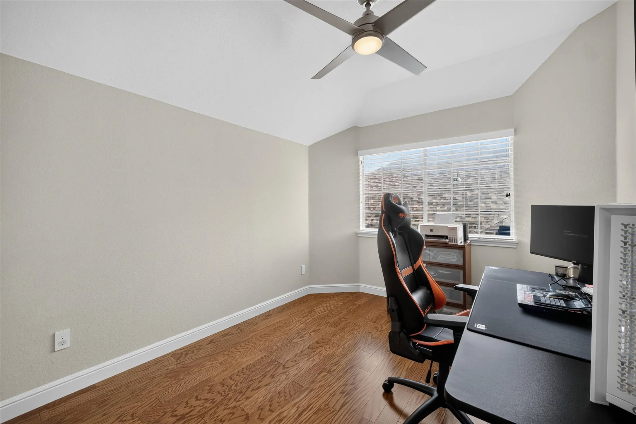 Vaulted ceiling with a ceiling fan, wood-finish flooring, and a large window with horizontal blinds