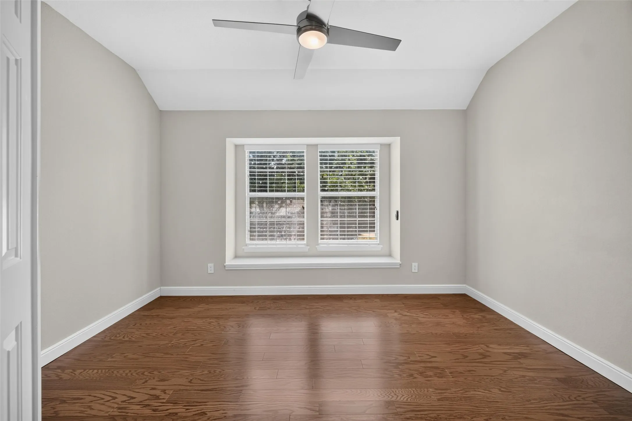 Vaulted ceiling with a flush-mount ceiling fan, rich wood-finish flooring, and a window with white blinds