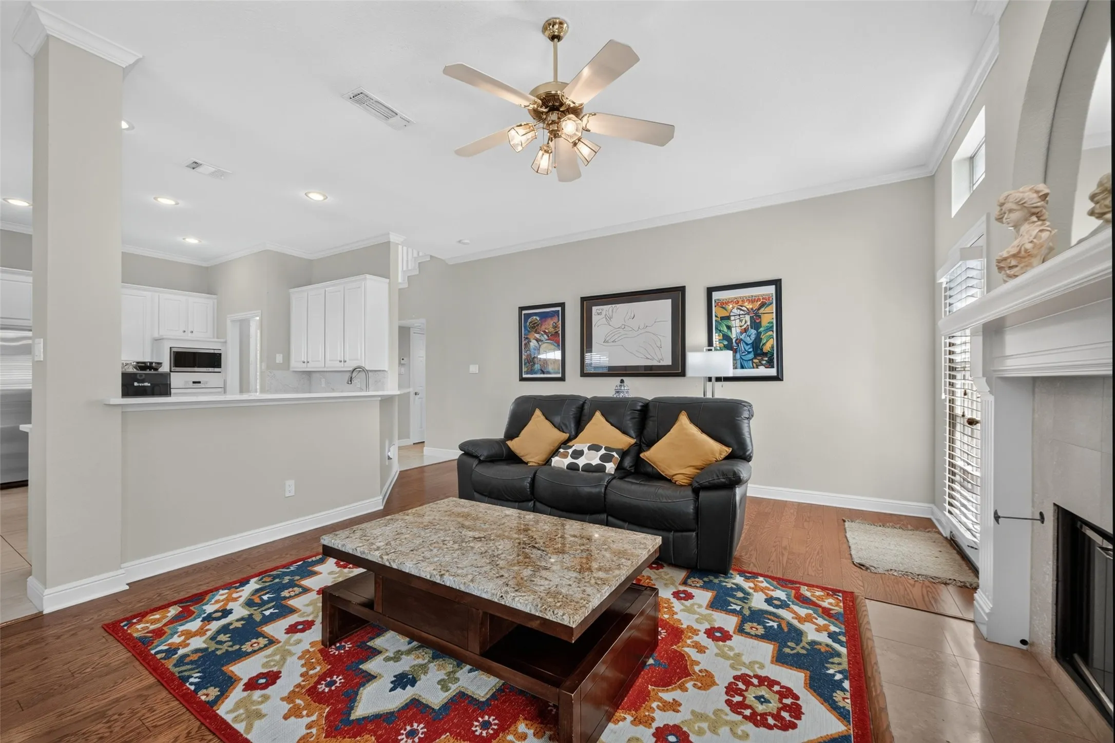 Open-concept living area featuring wood-finish flooring, a ceiling fan with integrated lighting, and a fireplace with a mantel