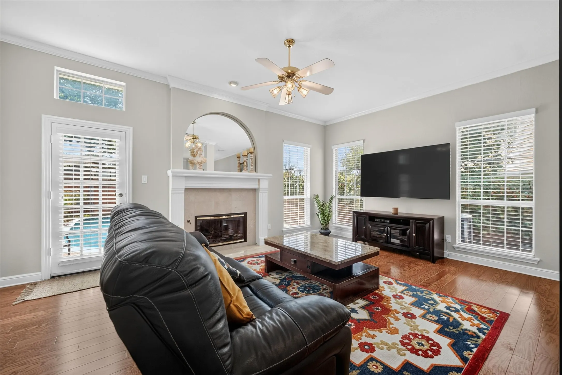 Hardwood flooring, fireplace with a mantel, ceiling fan with integrated lighting, multiple windows with blinds, and white trim throughout
