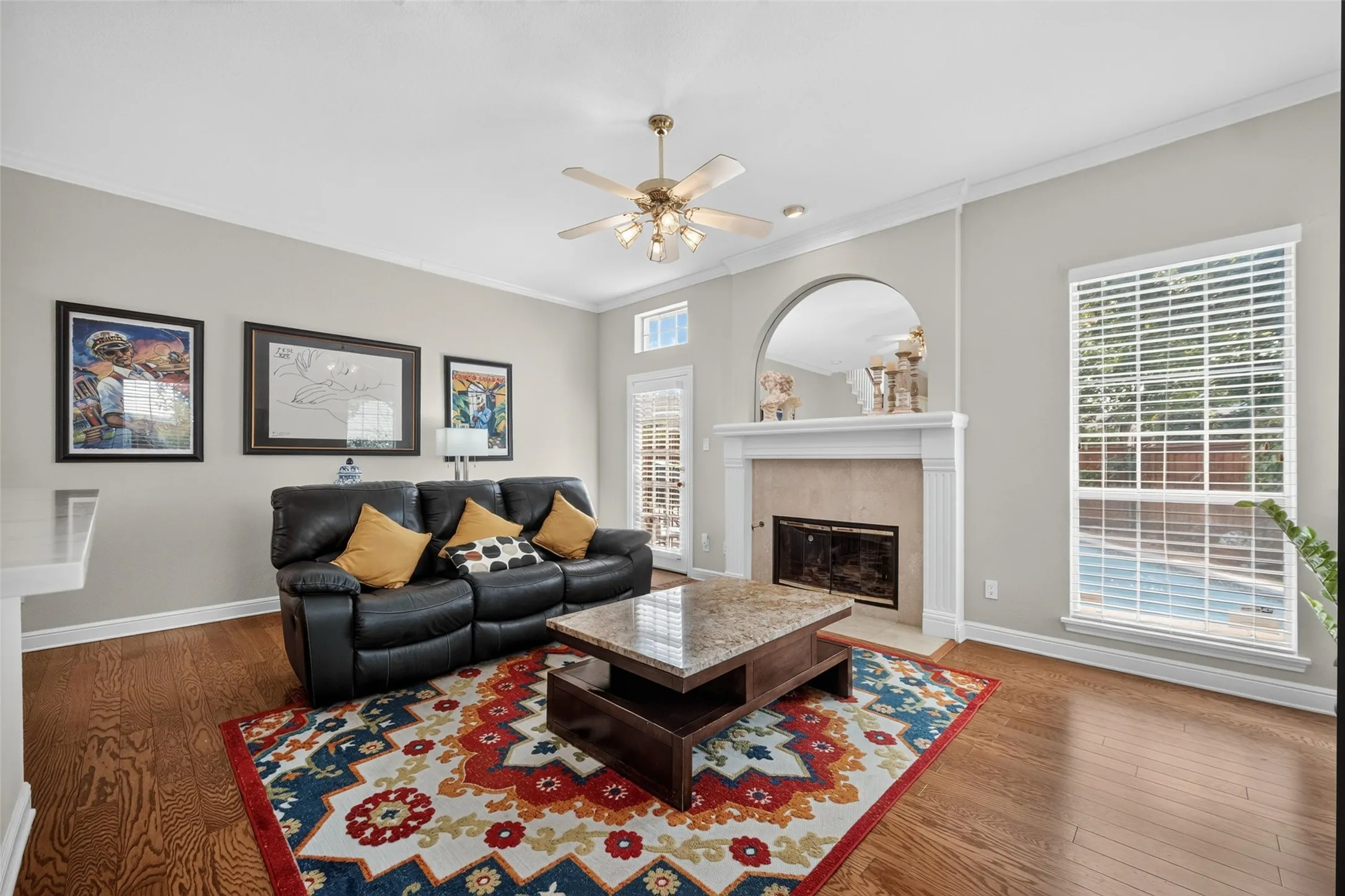 Hardwood flooring, fireplace with arched alcove, ceiling fan with integrated lighting, and crown molding