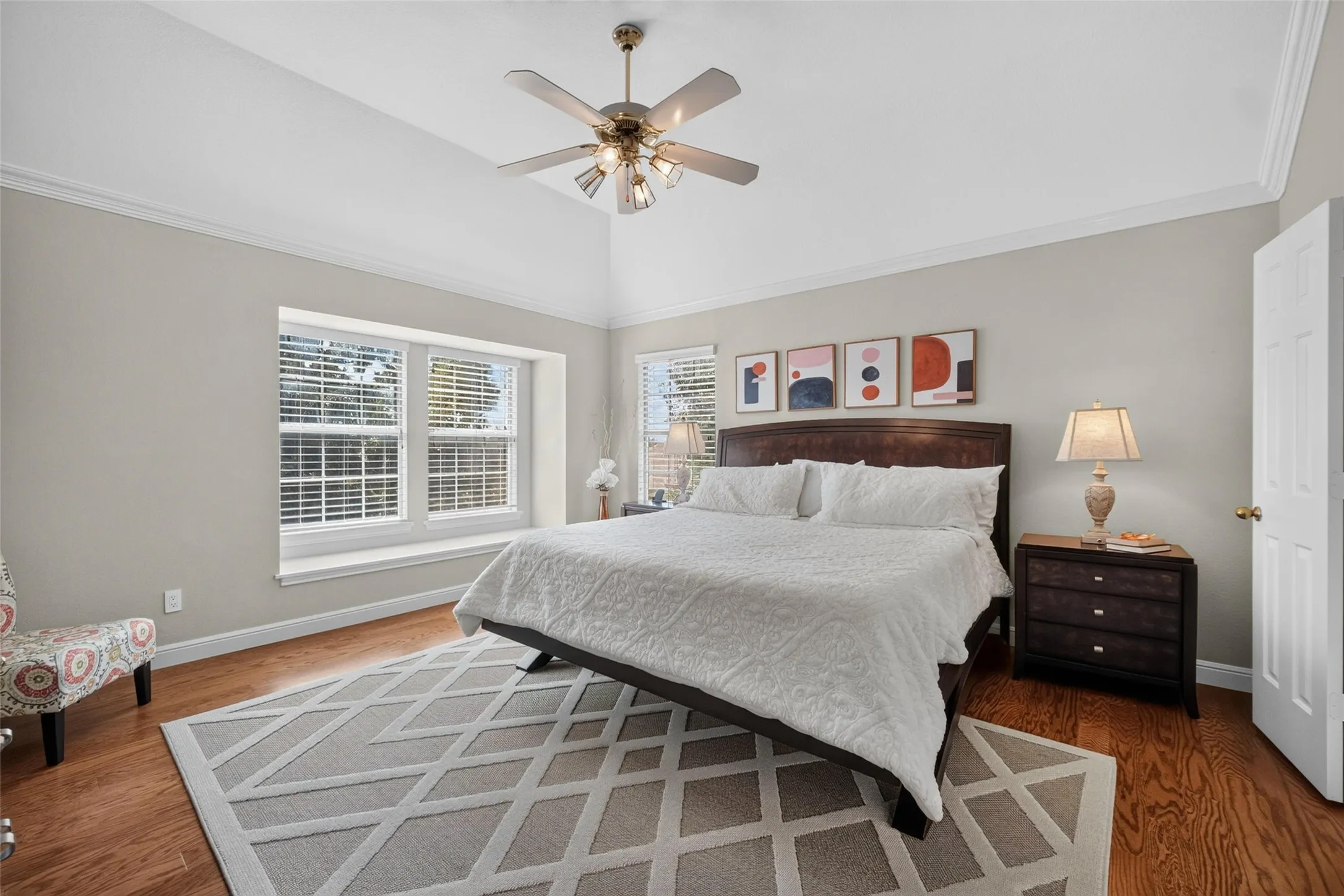 Vaulted ceiling with crown molding, wood-finish flooring, and a large window with a built-in sill