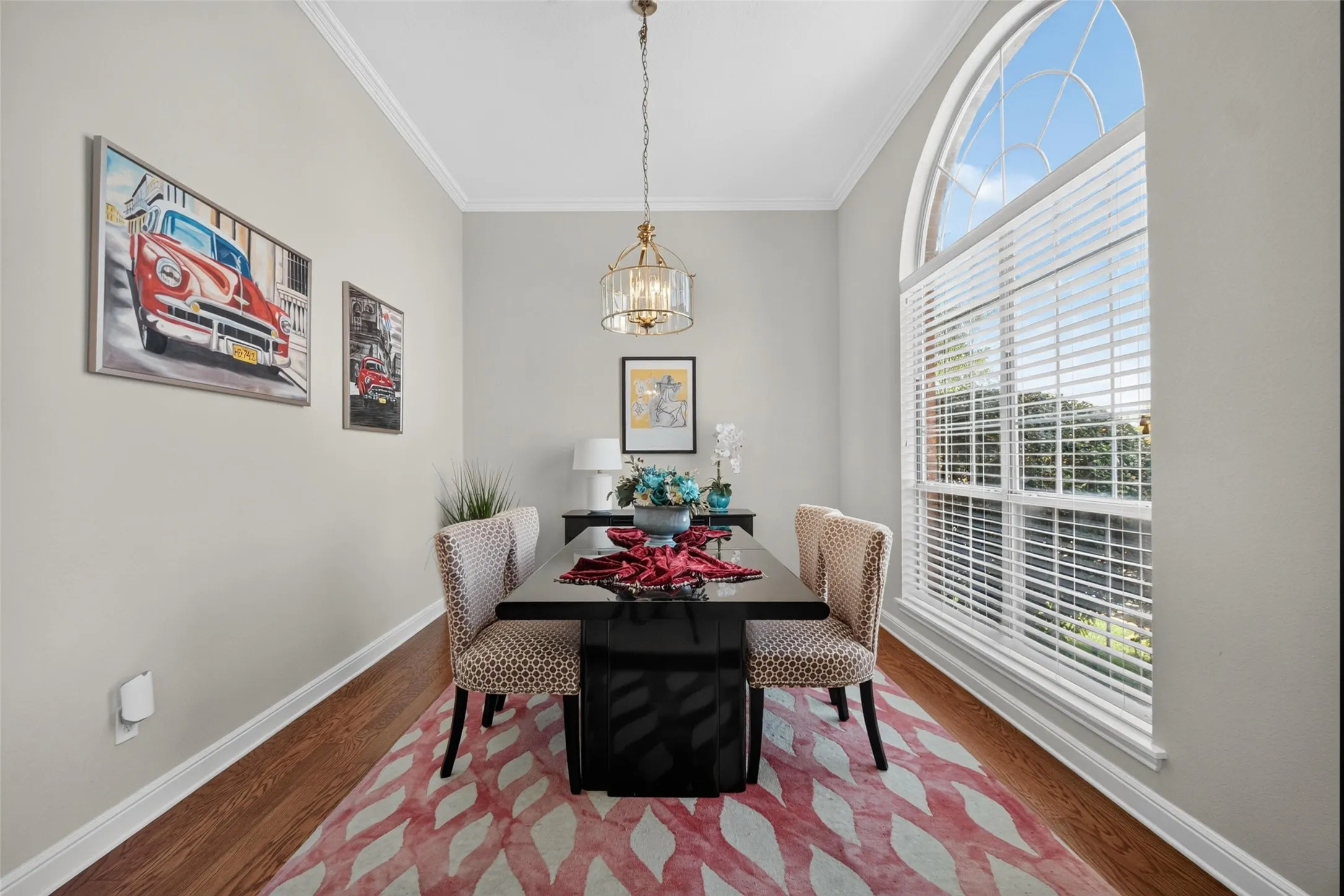 Wood-finish flooring, crown molding, and a tall arched window with blinds