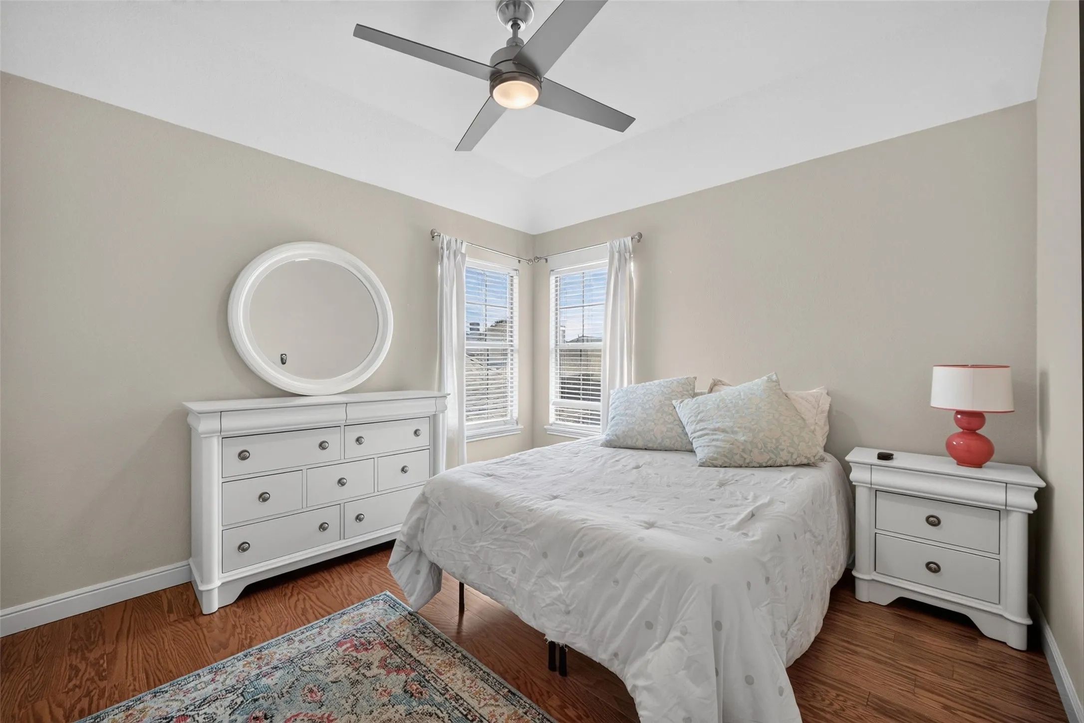 Vaulted ceiling with a ceiling fan, dual windows, wood-finish flooring, and light-toned wall paint