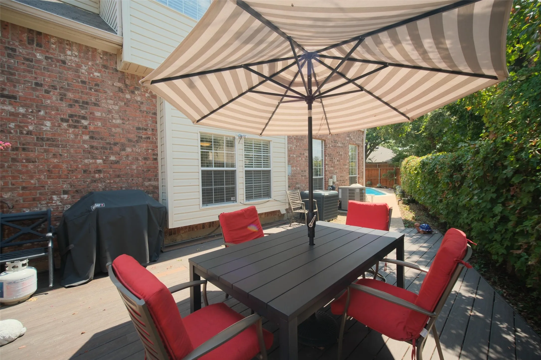 Wood-look composite decking, brick exterior, white siding, multiple windows, and a paved walkway