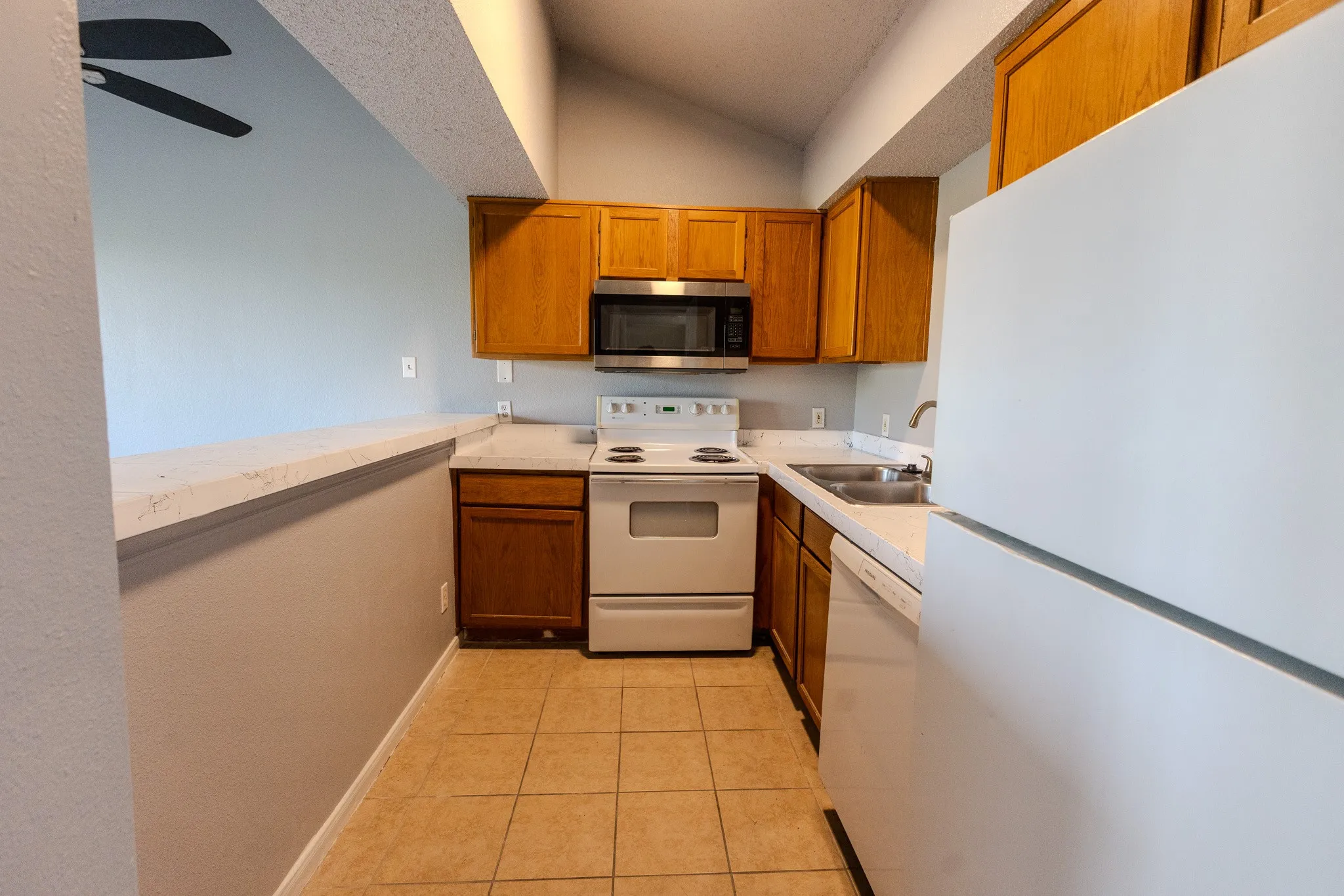 Kitchen featuring wood cabinetry, solid surface countertops, a stainless steel microwave, and tile flooring