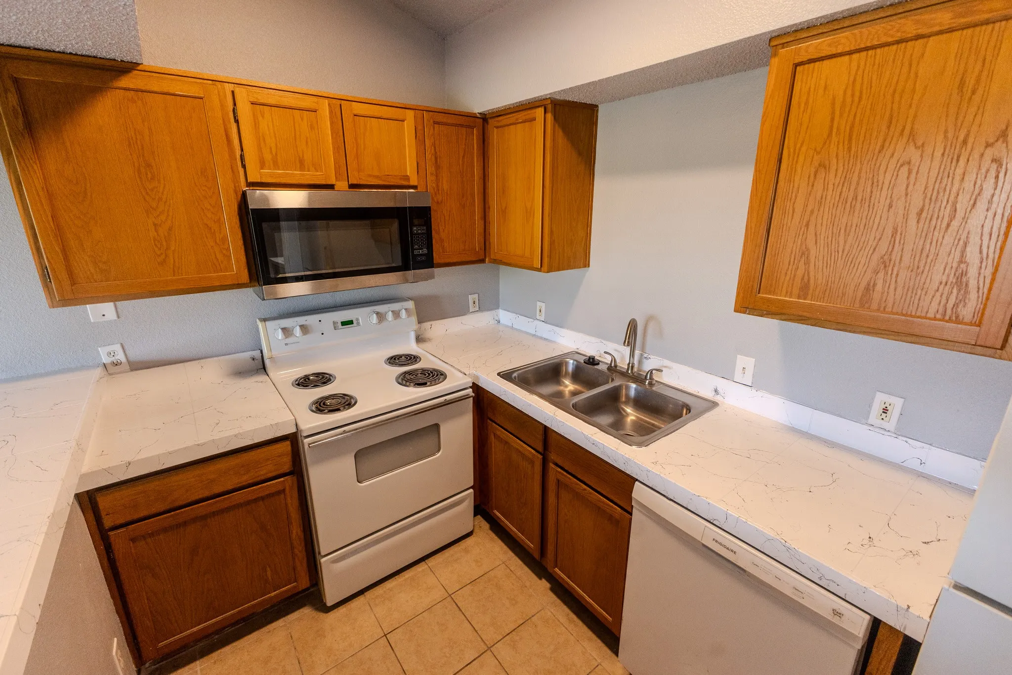 Kitchen featuring wood-finish cabinetry, light-toned countertops, and a dual basin stainless steel sink