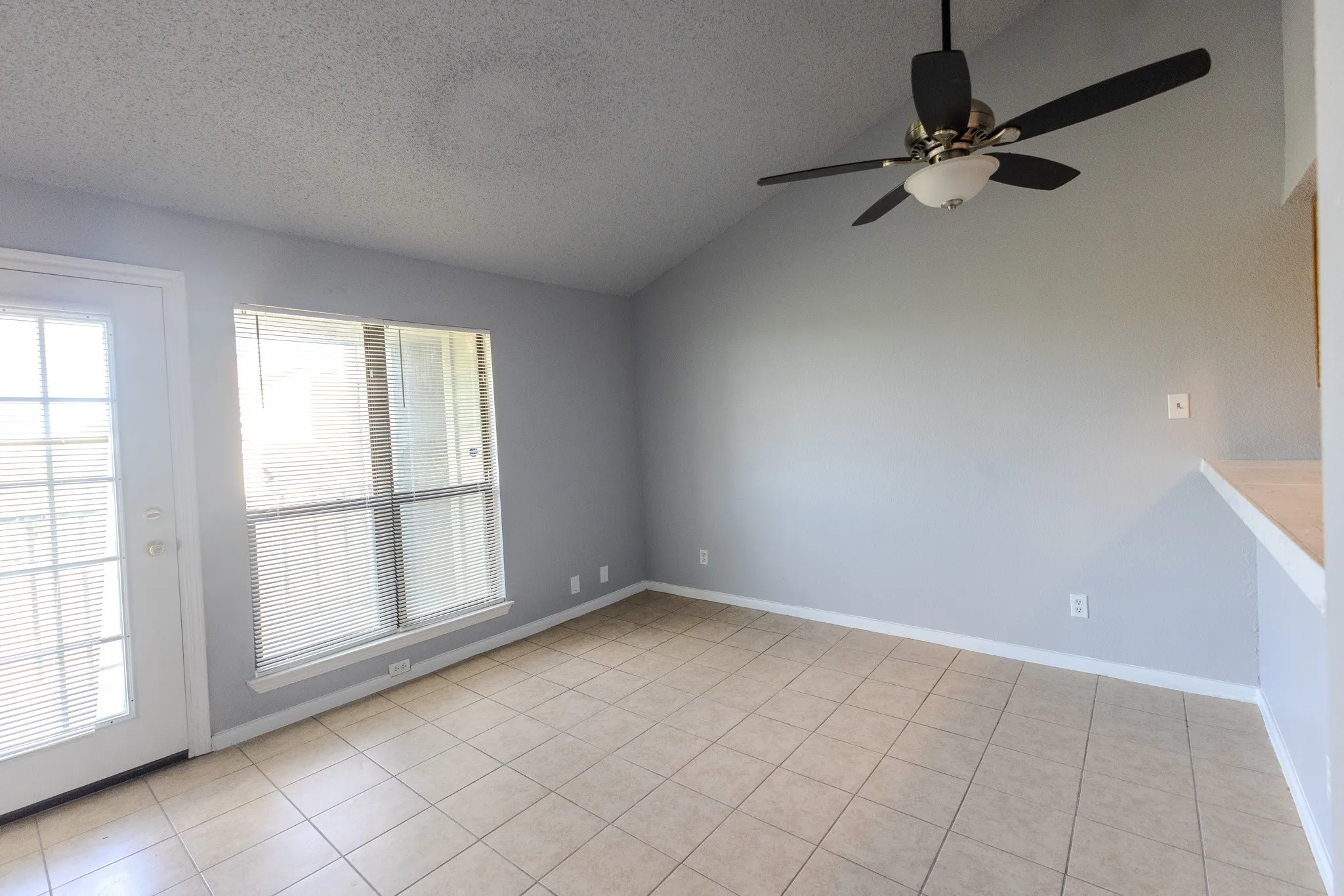 Vaulted ceiling with a ceiling fan, neutral tile flooring, window with blinds, and a glass-paneled exterior door